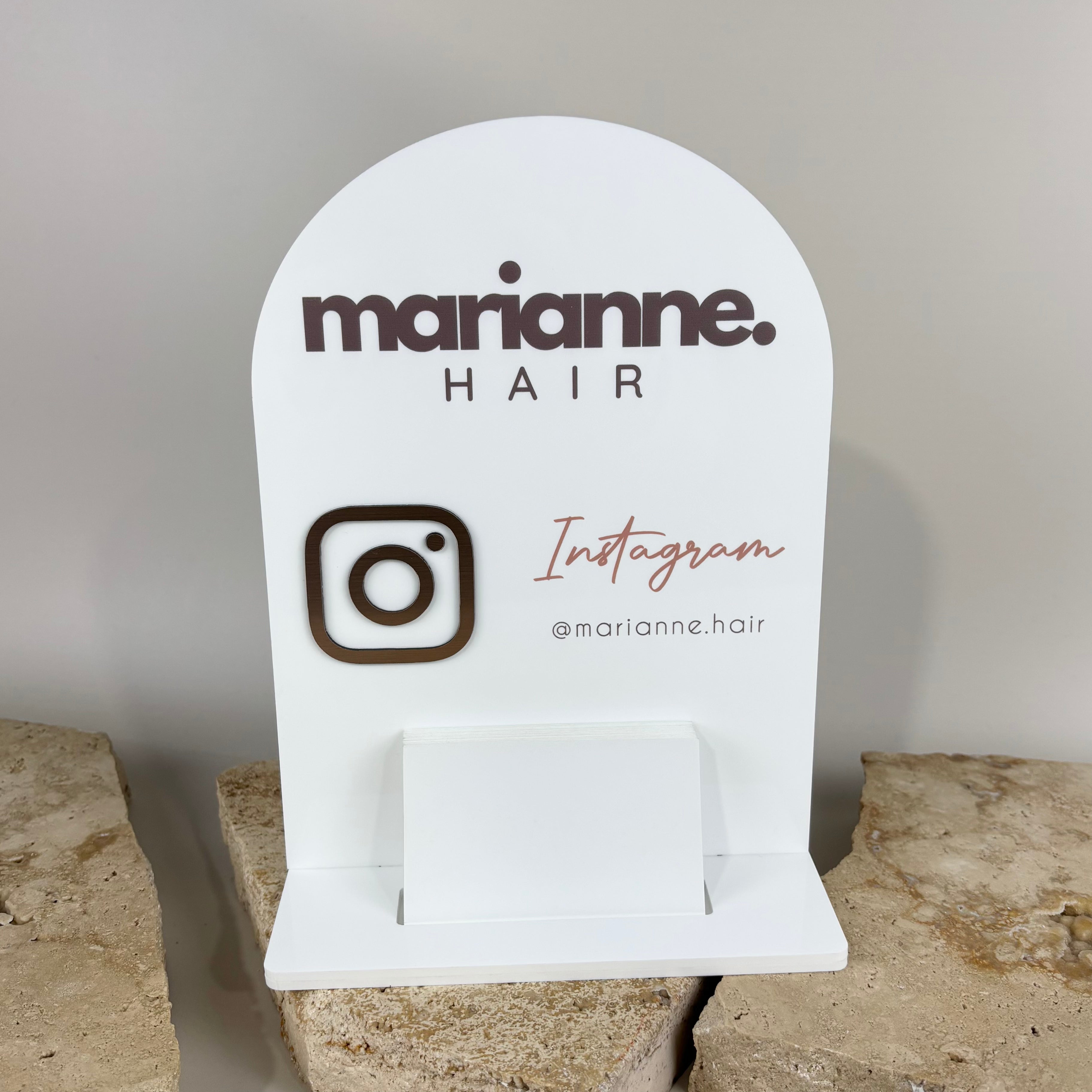 Custom acrylic Instagram business display stand for Marianne Hair, featuring a white arched design with 3D brown logo, Instagram icon, and pink script text. Includes a built-in card holder base. Perfect for salon counters and small business branding.