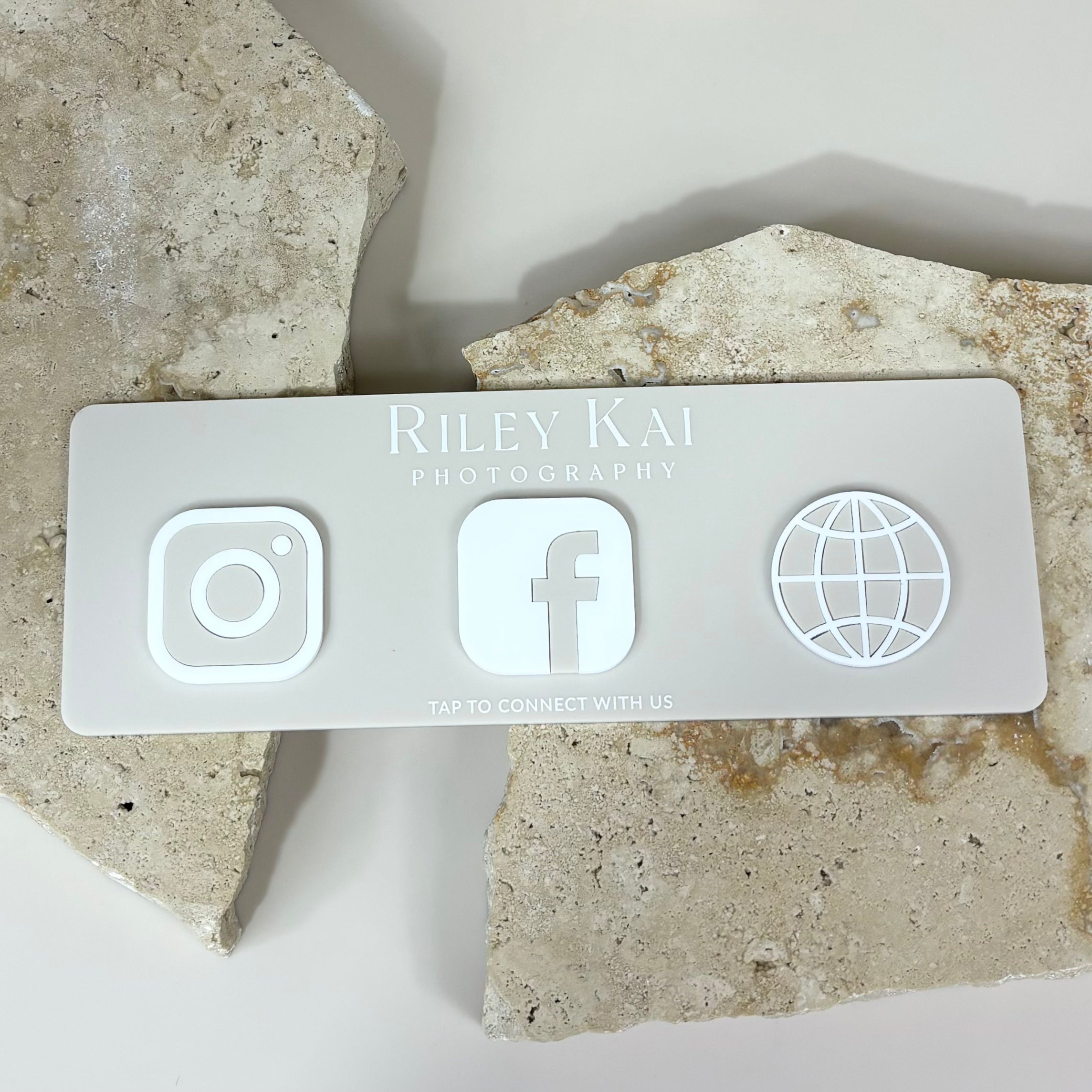 White NFC social plaque with Instagram, Facebook and website icons displayed on stone background.