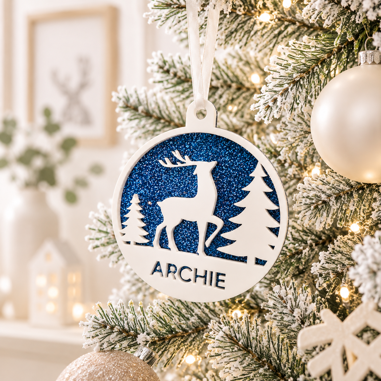 Personalised blue glitter acrylic Christmas bauble with white reindeer and pine tree design, custom name ornament for Christmas tree décor.