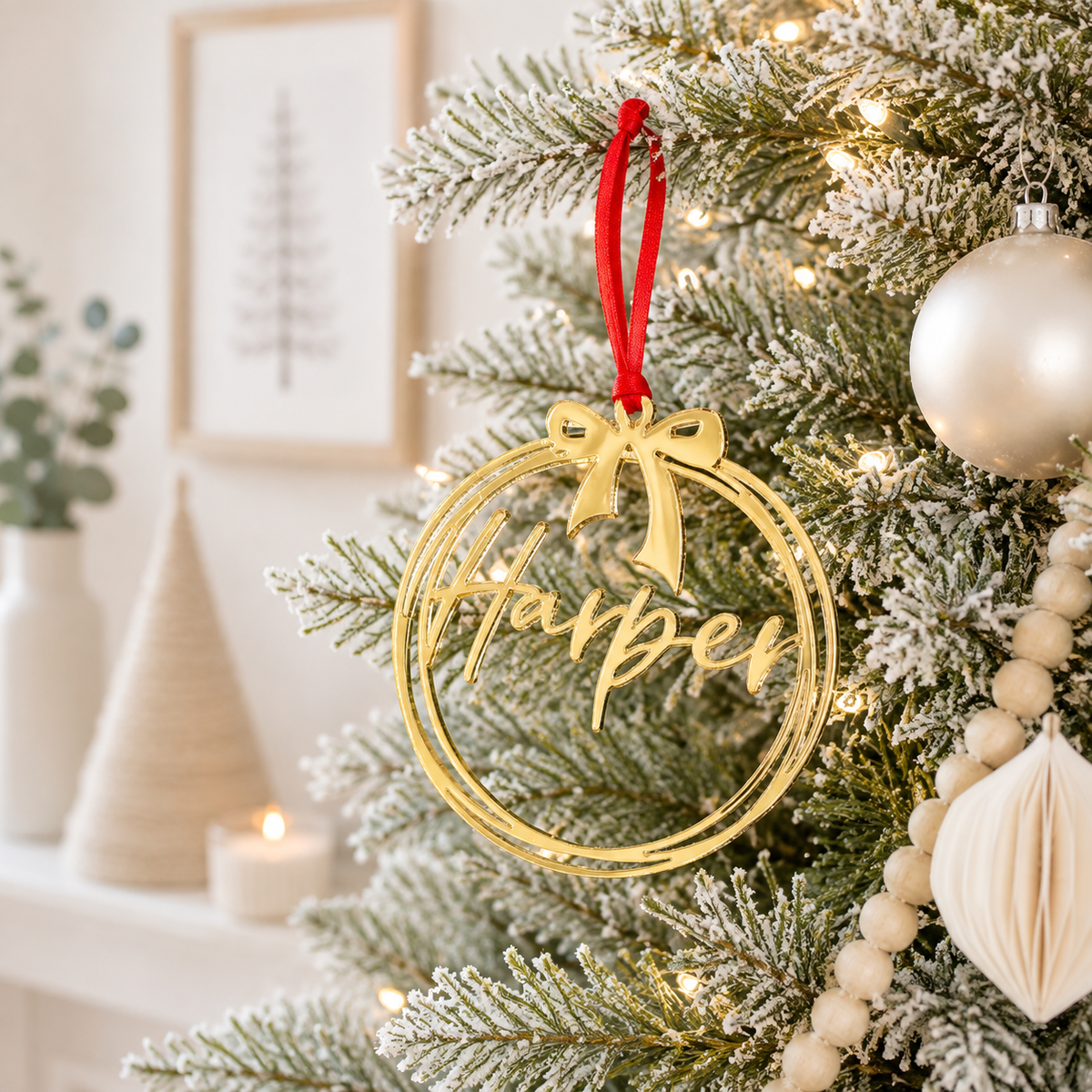 Personalised gold mirror acrylic Christmas bauble with custom name and bow design, hanging on a modern frosted Christmas tree.