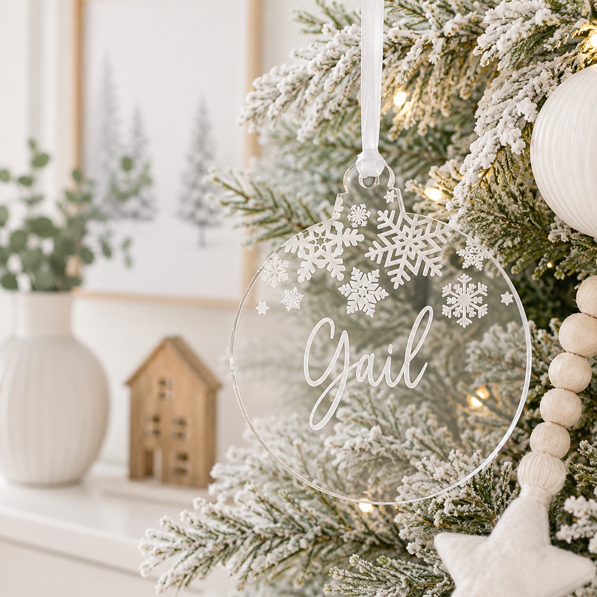 Personalised clear acrylic Christmas bauble with custom name and engraved snowflake design, hanging on a modern frosted Christmas tree.