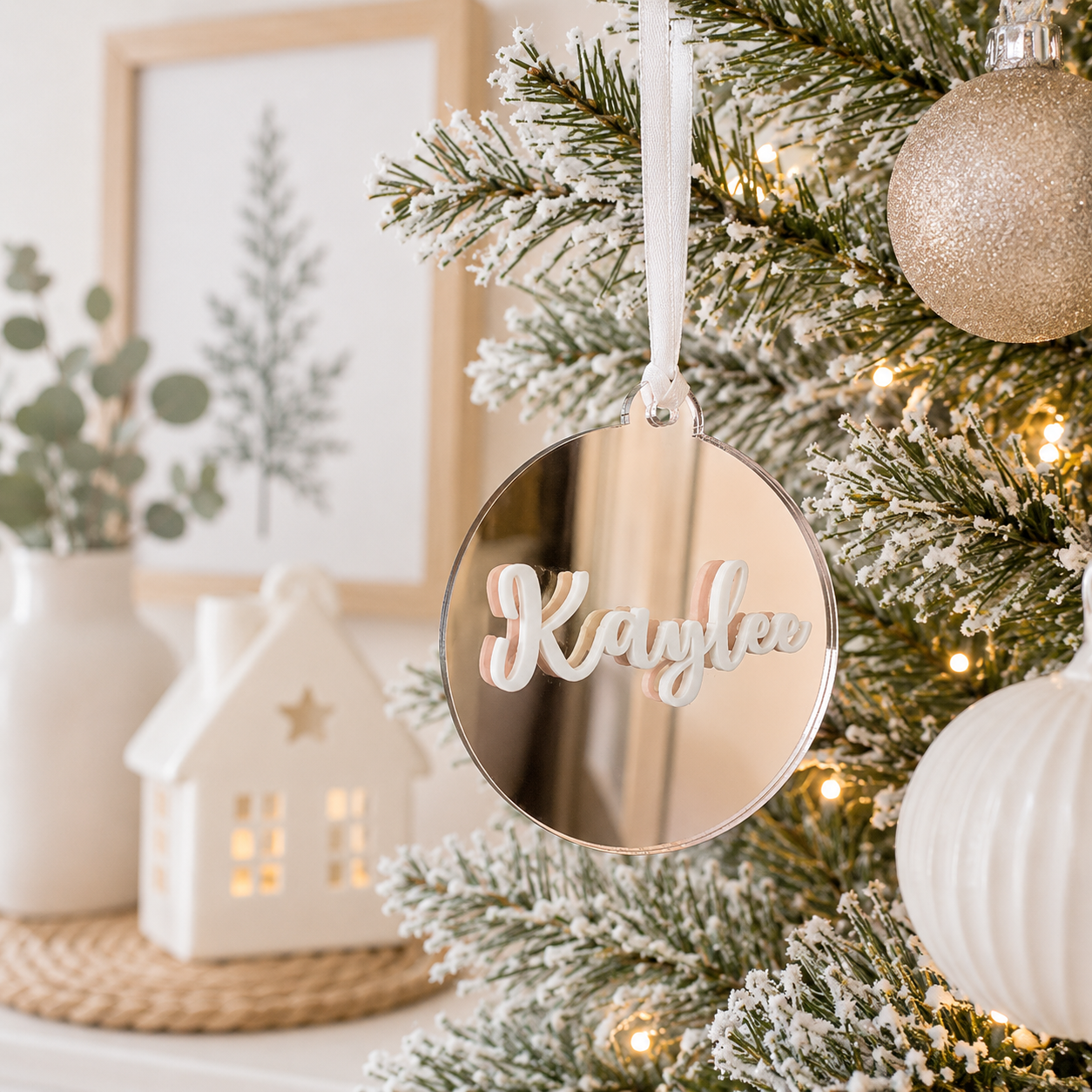 Personalised rose gold mirror acrylic Christmas bauble with custom raised white name, hanging on a modern frosted Christmas tree.