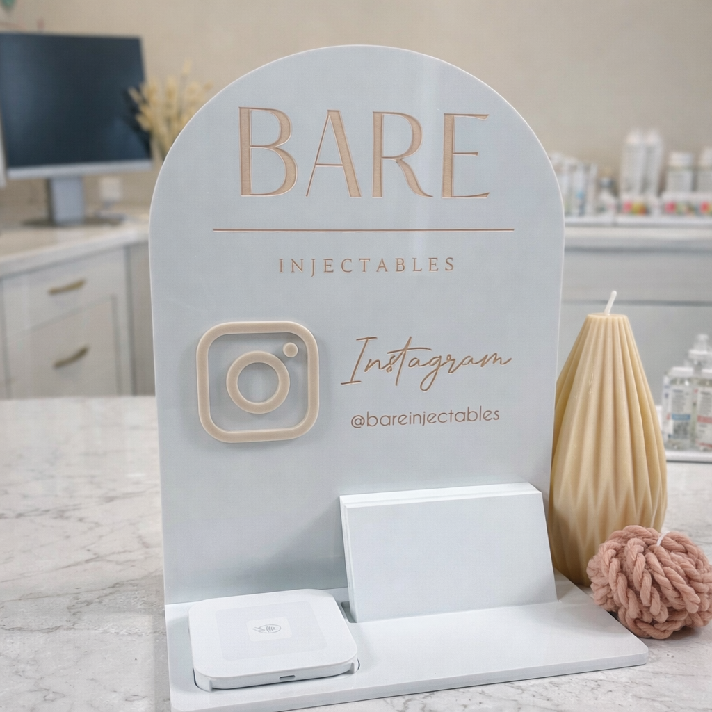 Branded acrylic NFC social media stand for cosmetic injectable clinic on a reception counter with Instagram signage and phone charging station