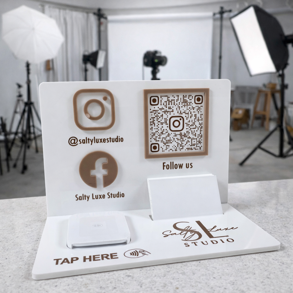 Custom acrylic NFC business stand for photography studio displayed on a studio counter, featuring Salty Luxe Studio branding, Instagram and Facebook details, QR code, business card holder and square reader device for tap payments