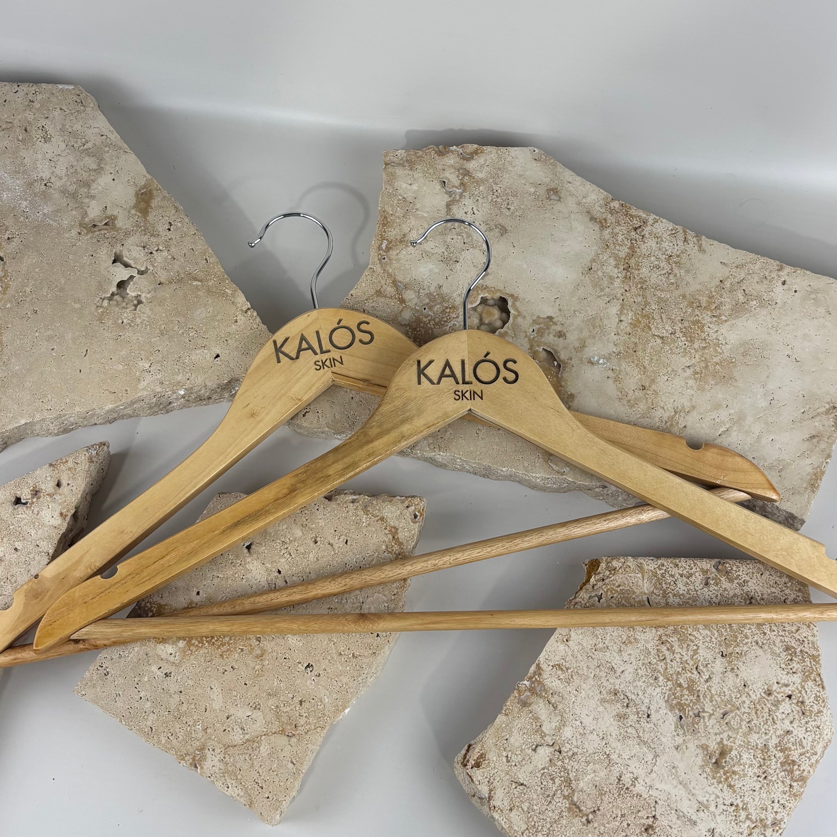 Custom engraved wooden coat hangers with logo, personalised timber hangers for business branding, bamboo clothes hangers with UV printed logo KALÓS SKIN, boutique retail display hangers Australia, salon and clinic branded hangers, sustainable wooden garment hangers with metal hook, custom business merchandise hanger set