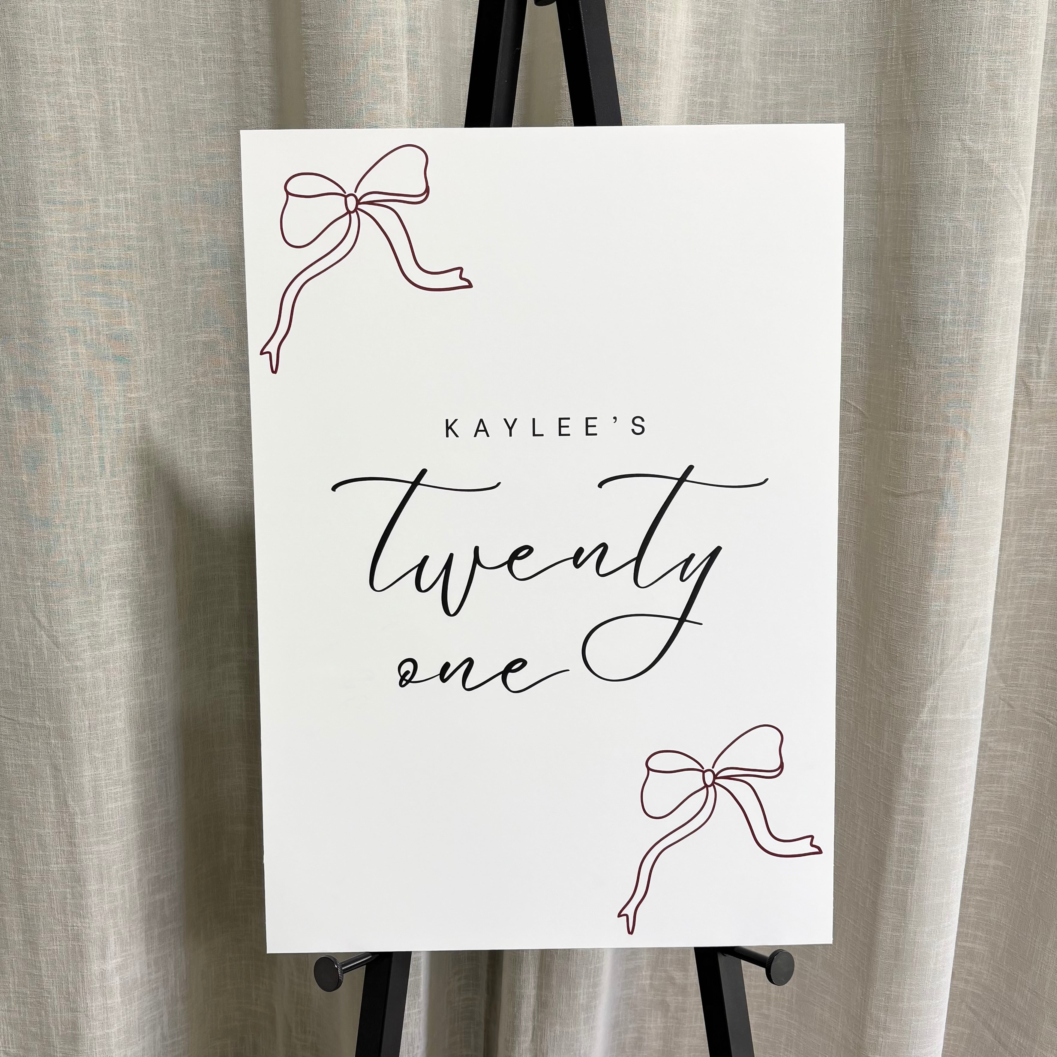 Custom cardboard birthday sign, “Kaylee’s twenty one” event welcome board, lightweight foam board party signage Australia, personalised 21st birthday sign with bow design, affordable event display sign on easel, printed milestone birthday welcome sign for parties and celebrations