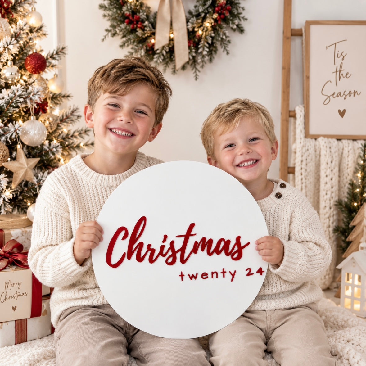Christmas photo prop sign with red acrylic lettering, held by two children in a light, bright modern Christmas setting.