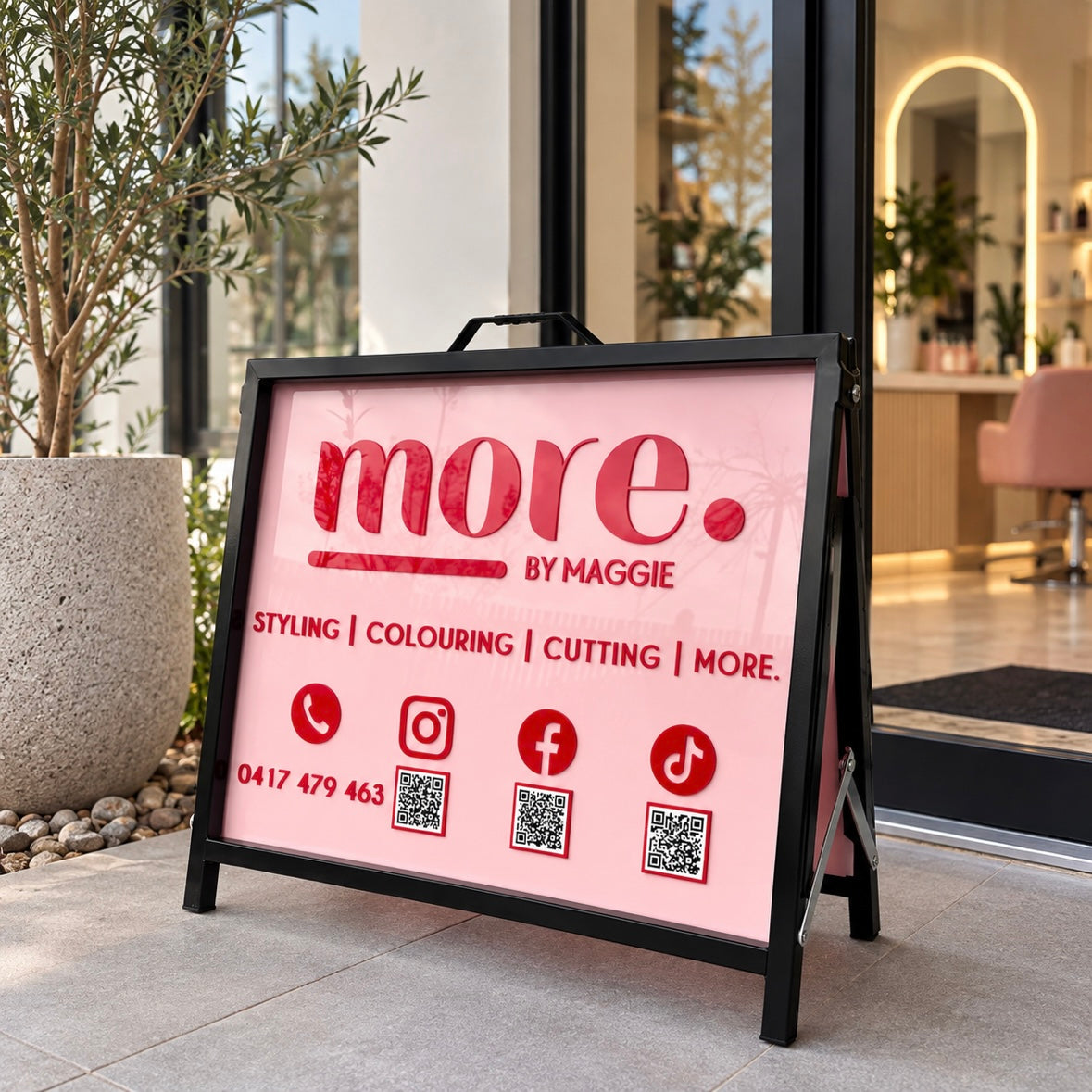 Custom 45x60cm pink hair salon A-frame sign with 3D acrylic lettering, social media icons and QR codes displayed outside a salon entrance.
