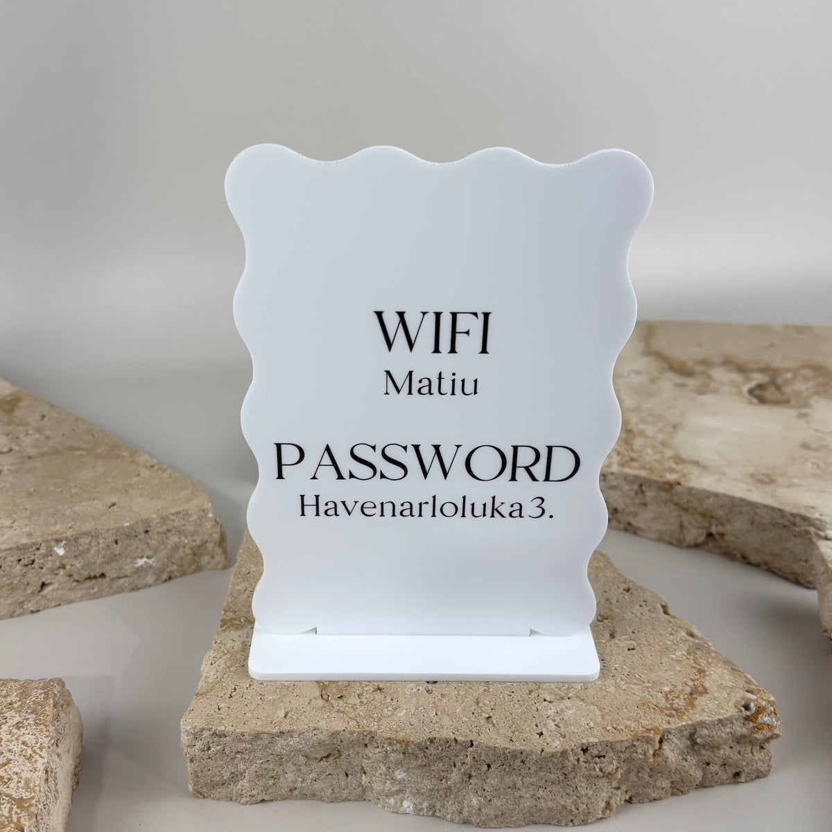 Personalised white acrylic WiFi password sign with scalloped edges and black text, displayed on a countertop stand.