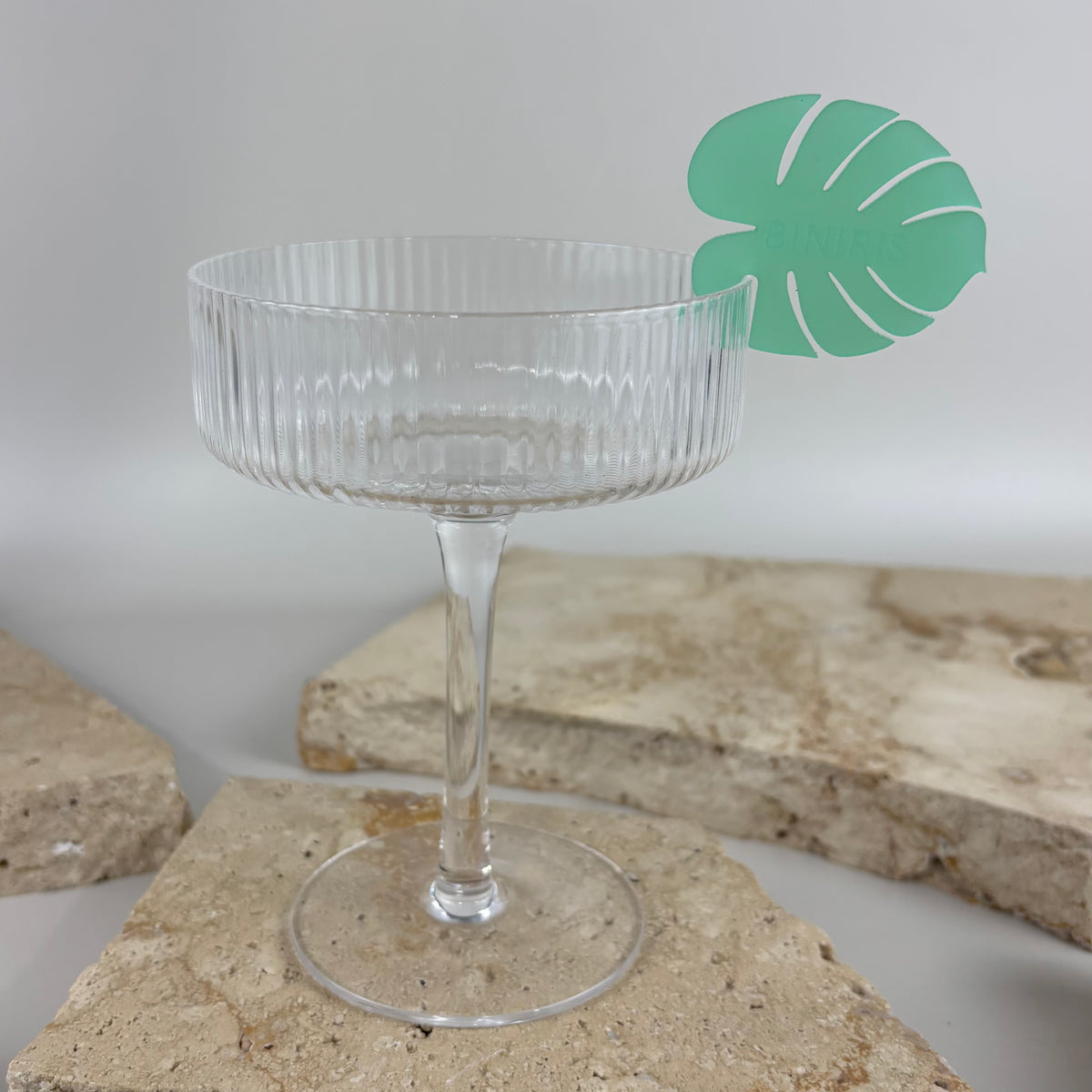 Green tropical leaf acrylic drink stirrer displayed in a clear cocktail glass.