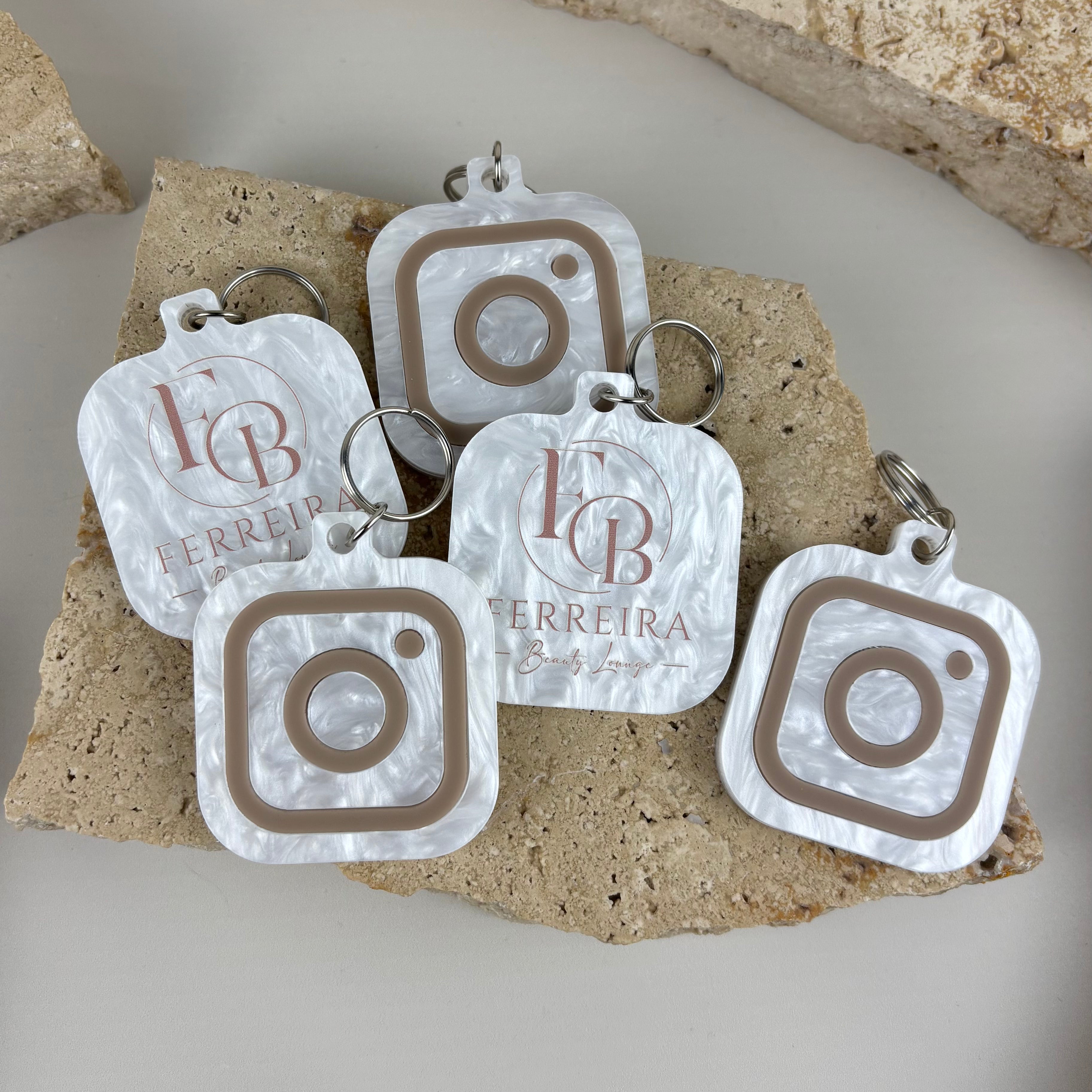 Personalised acrylic Instagram keychains featuring custom business logos and social media icons, made from white pearl acrylic with neutral raised details.