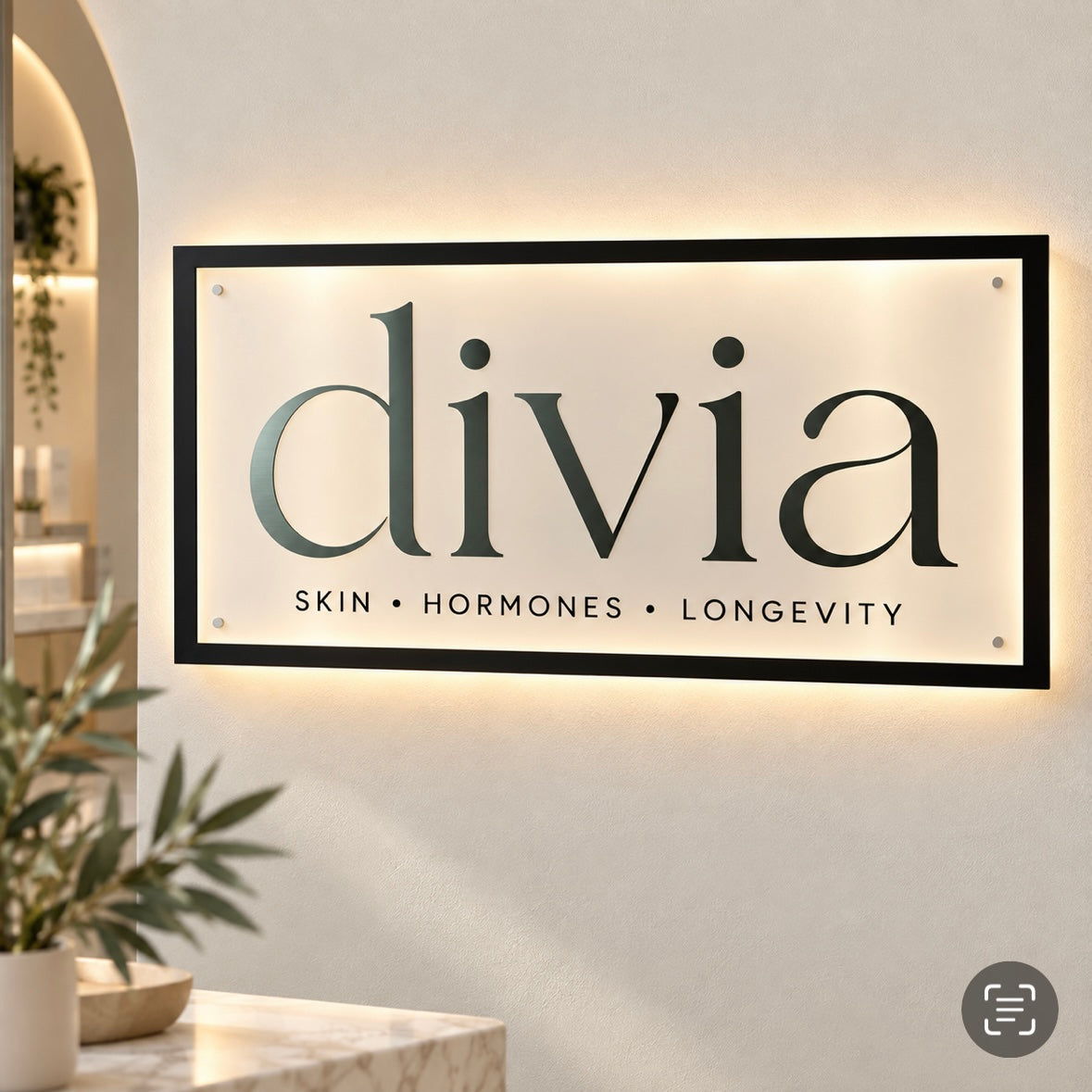 Custom rectangular LED backlit business sign with black frame and Divia Skin Hormones Longevity branding, mounted on a modern wellness clinic wall.