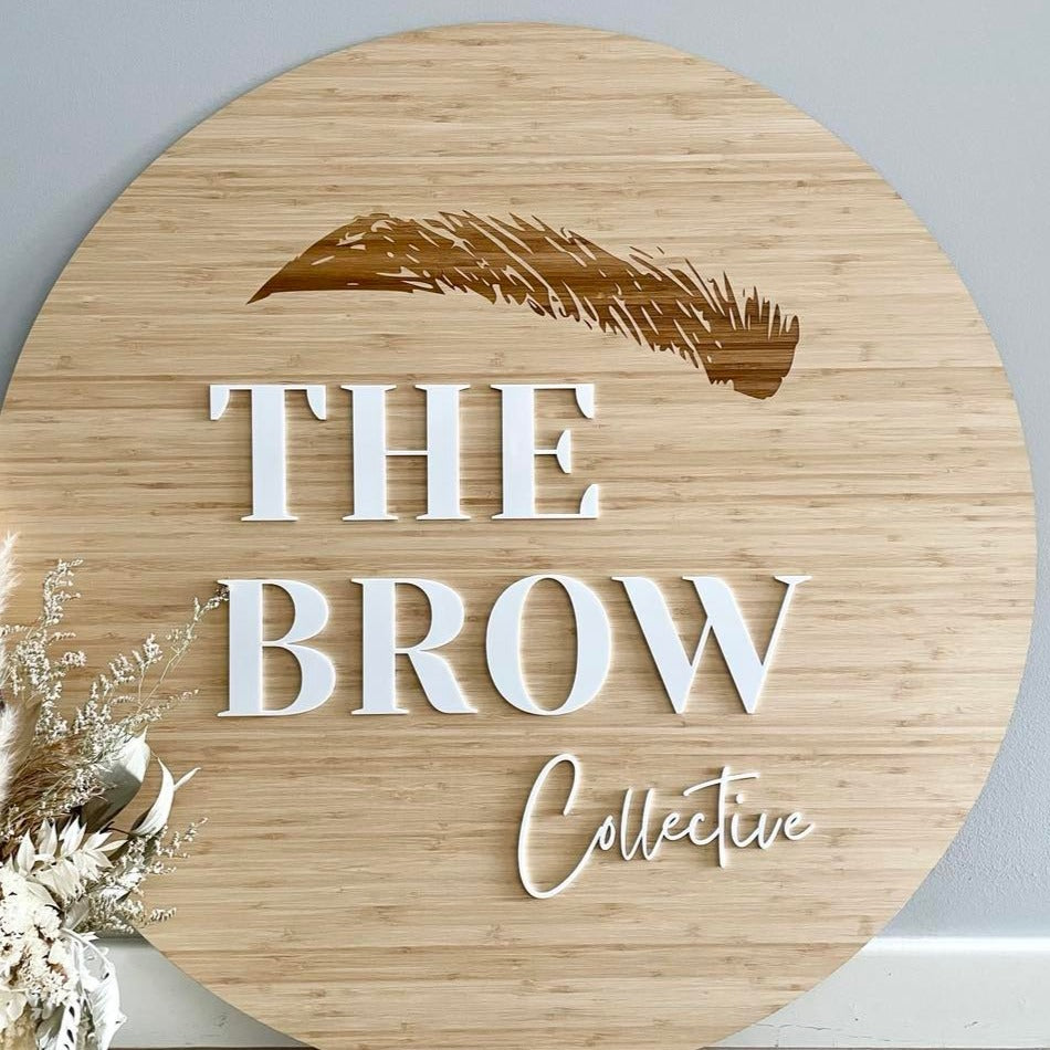 The Brow Collective bamboo sign with bold white acrylic letters and feather detail