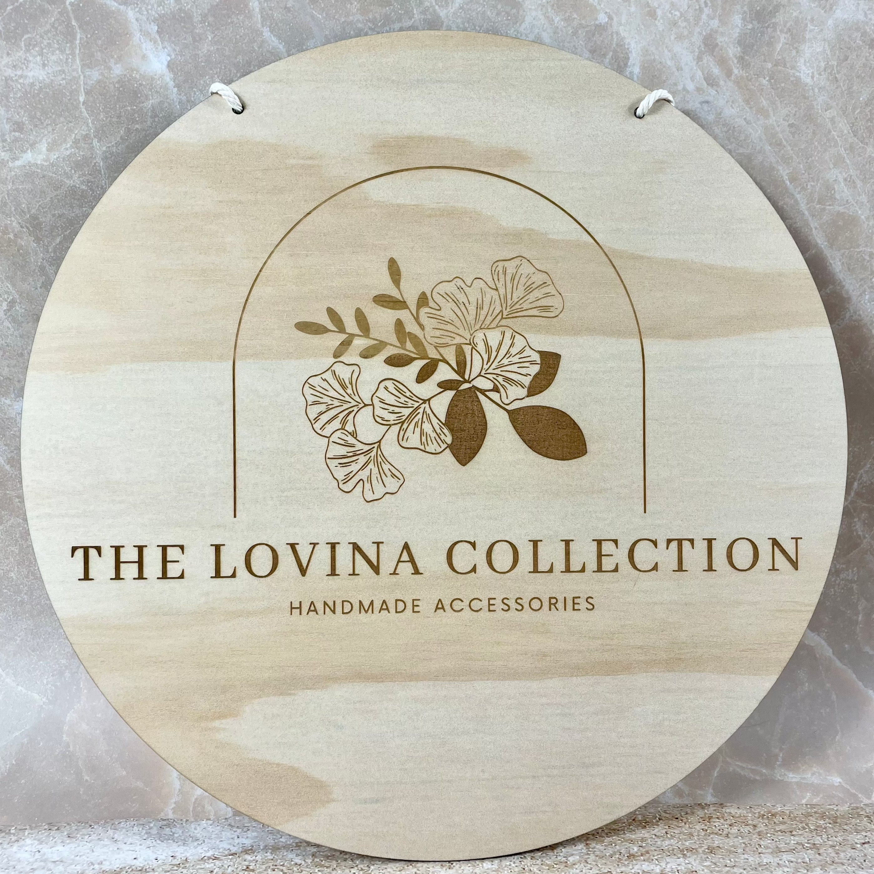 The Lovina Collection wooden shop sign, second variation of engraved timber branding with floral line art and business text.