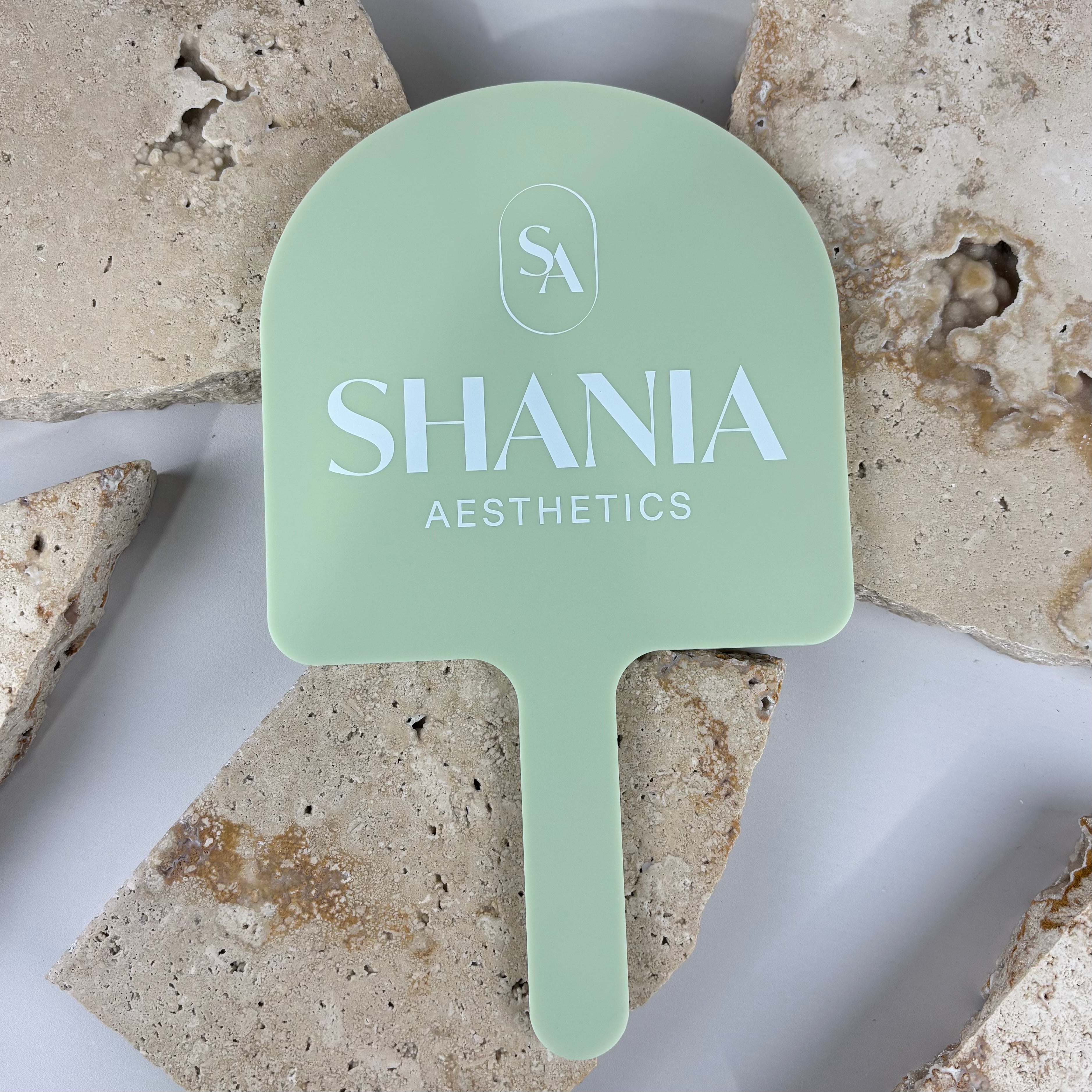 Custom pastel green acrylic handheld mirror with white logo and text, personalised beauty salon mirror for aesthetics clinic, branded handheld mirror for professional client photos and marketing