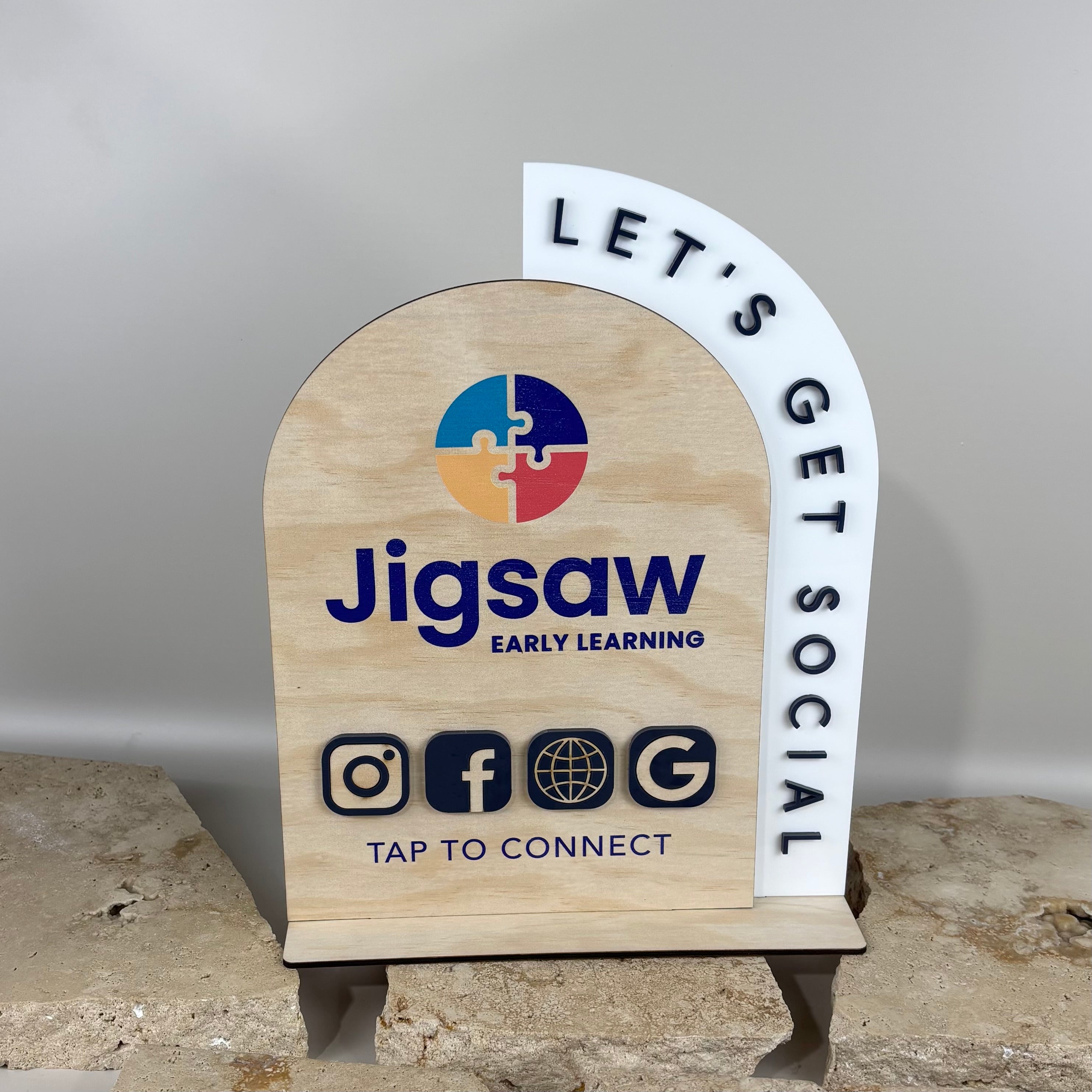 Custom timber and acrylic NFC business station with arched wooden panel and white acrylic side feature, branded for Jigsaw Early Learning, featuring social media icons and tap-to-connect function for childcare centres and education businesses.