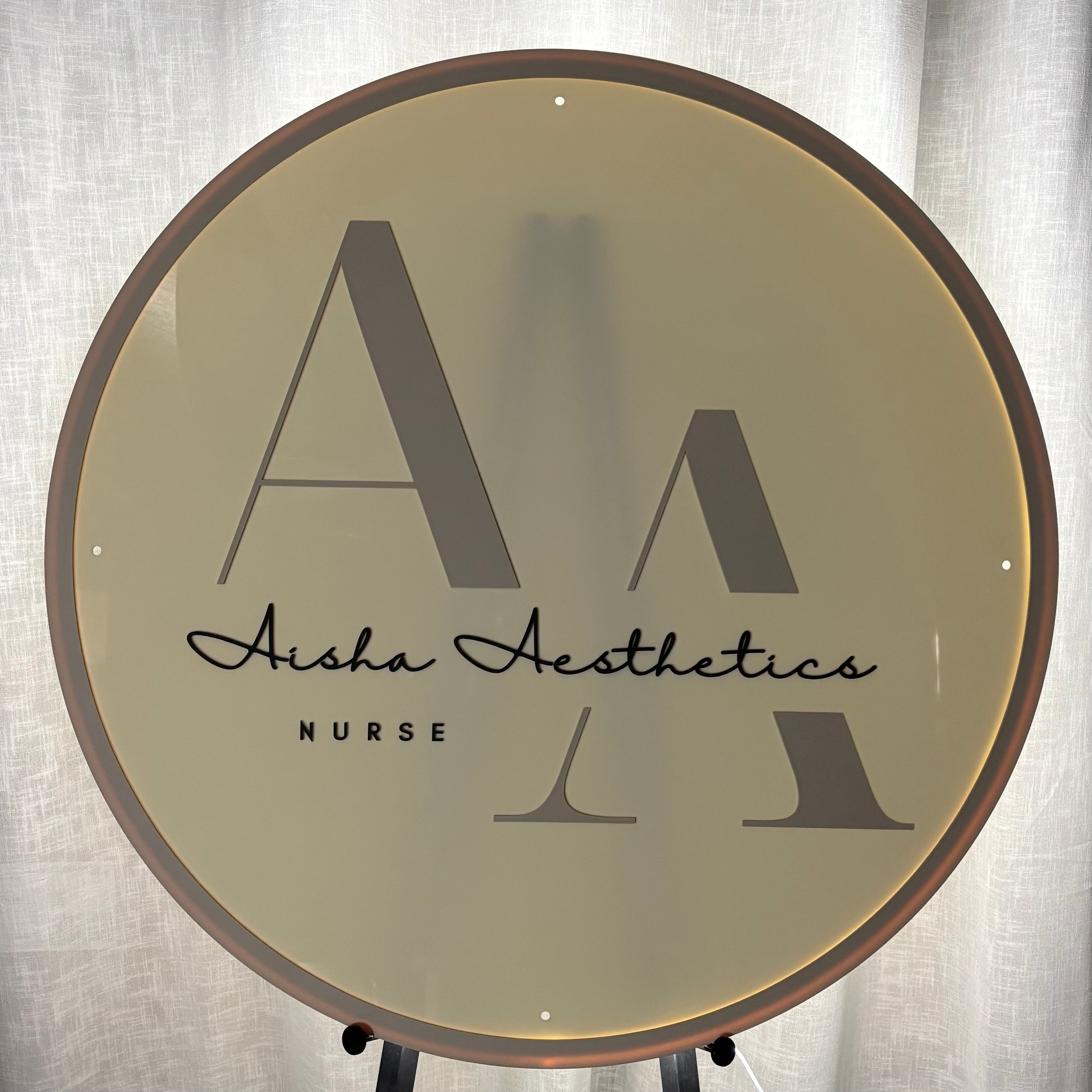 Backlit round acrylic business sign with UV printed logo for Aisha Aesthetics Nurse, featuring warm white LED halo lighting, premium acrylic face and modern custom salon signage for clinics, beauty salons and cosmetic businesses.