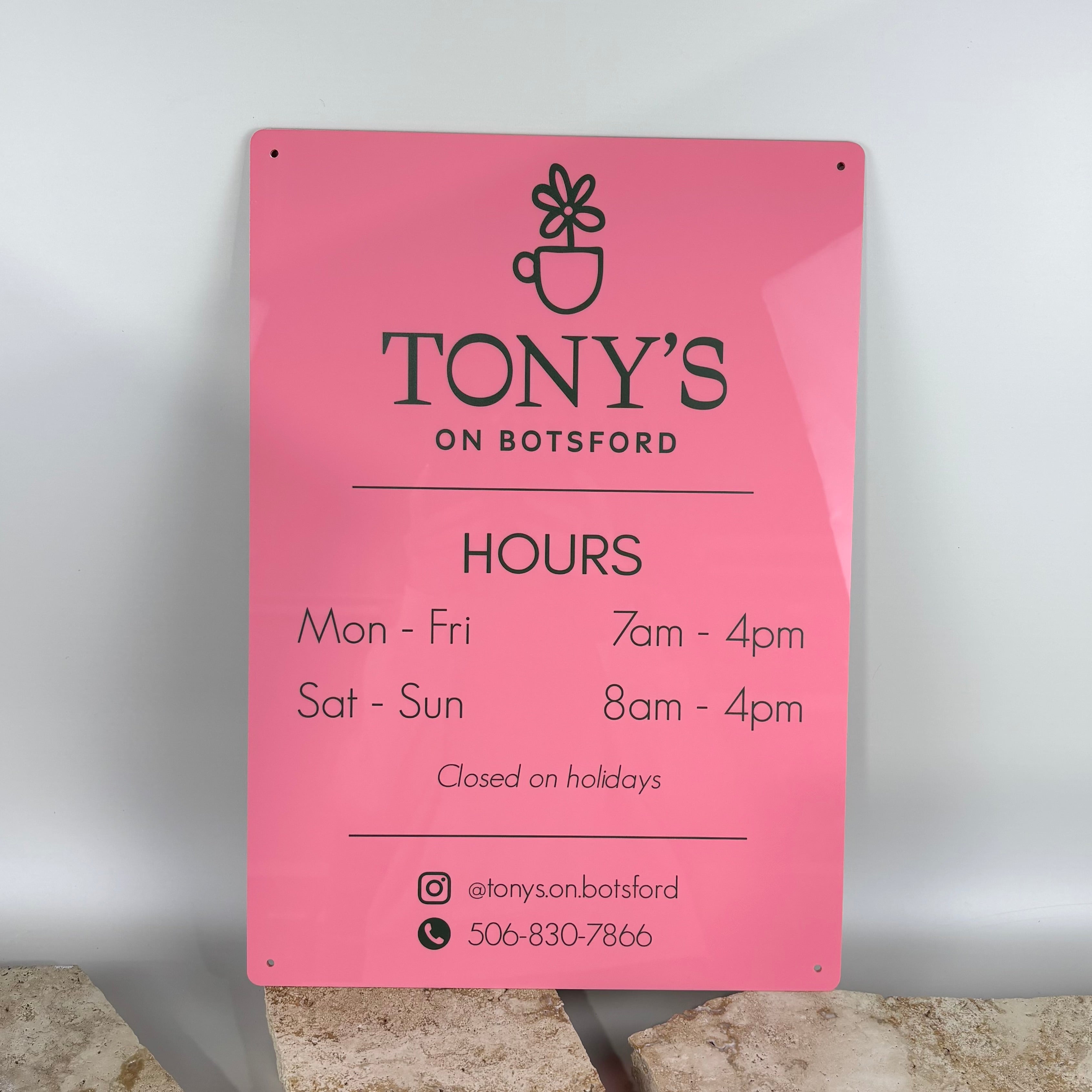 Custom pink acrylic business hours sign for Tony’s on Botsford café, featuring opening times, social media handle and phone number, with black printed text and rounded corners, displayed against a neutral backdrop.