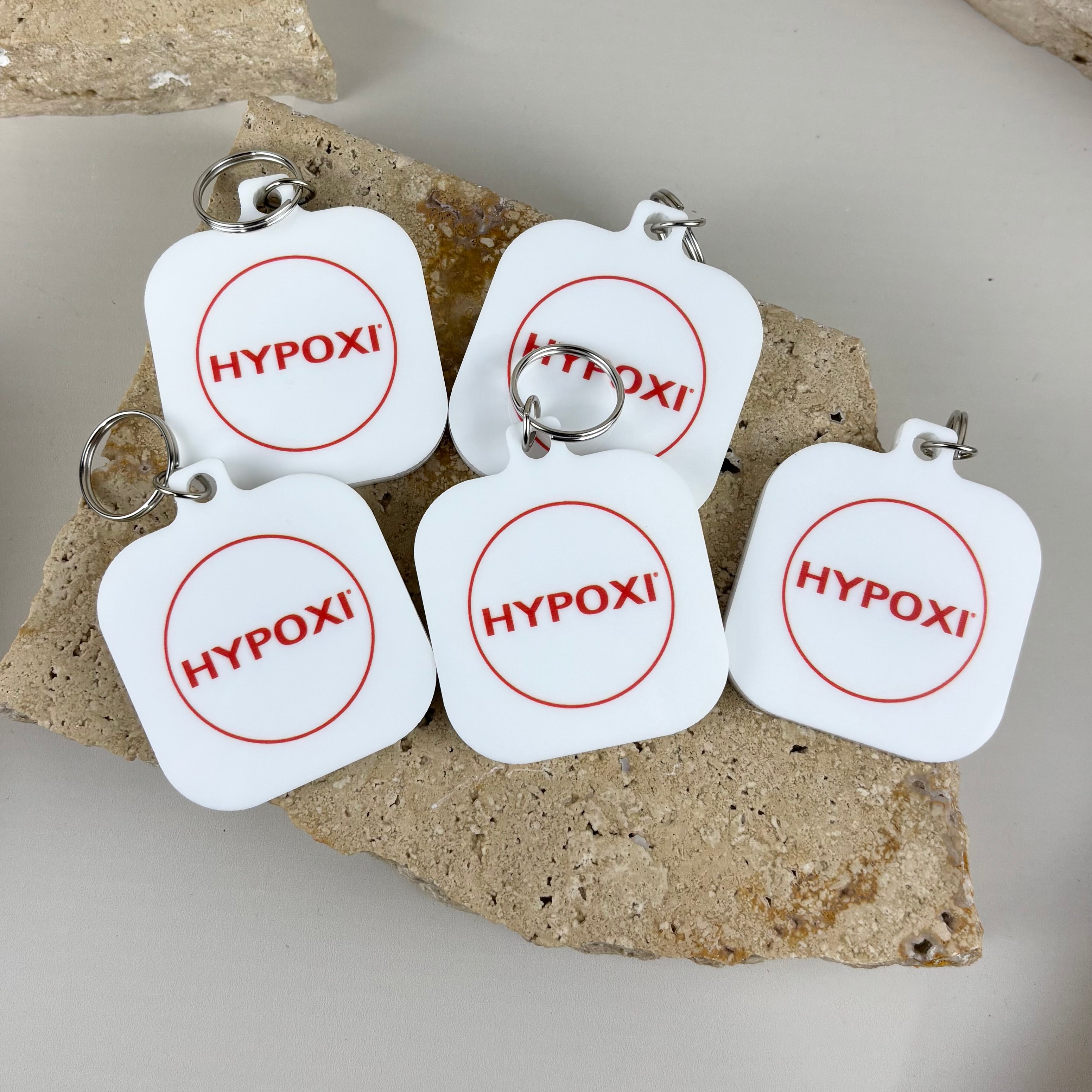 Custom white acrylic NFC keychains with UV printed red HYPOXI business logo for contactless digital access.