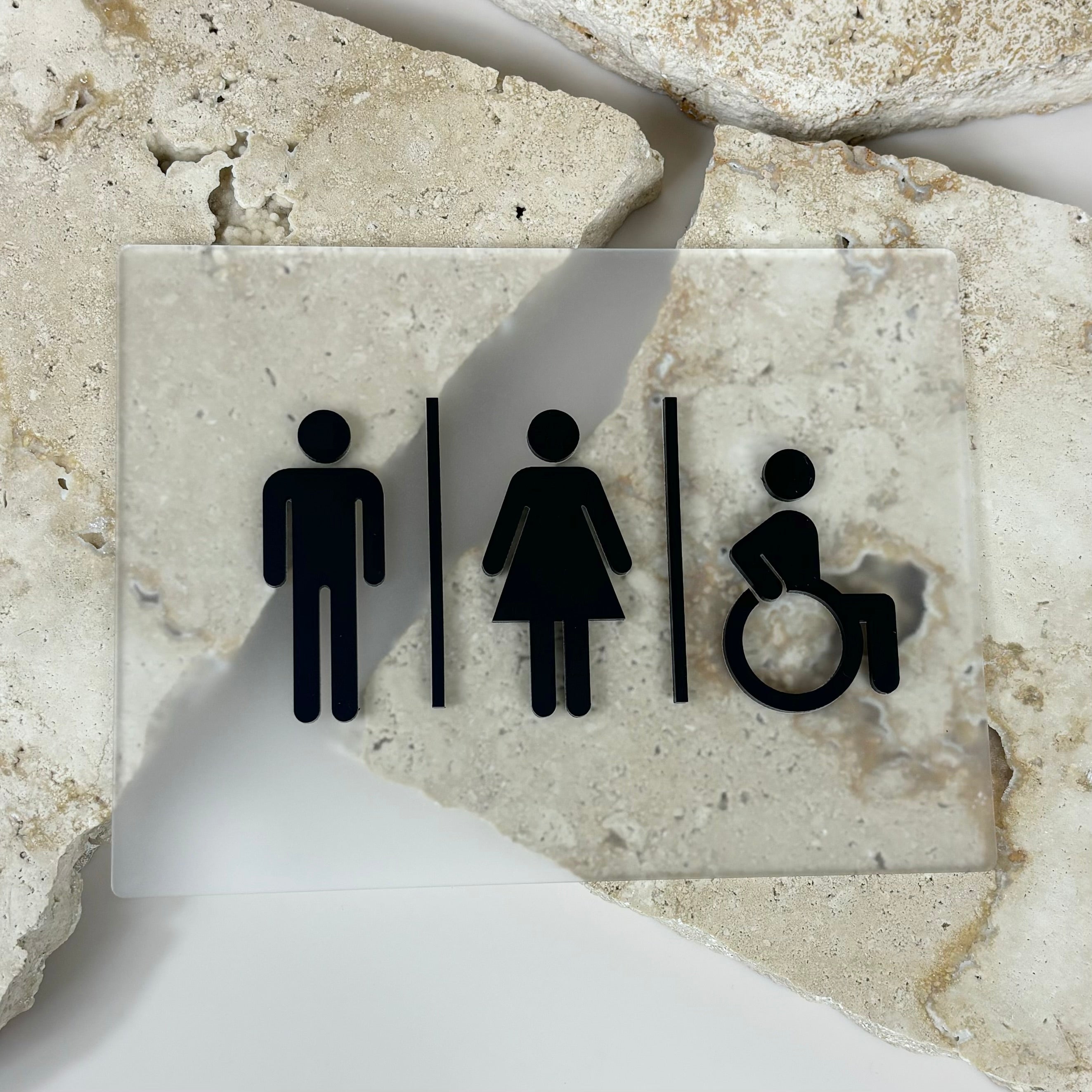 Close‑up of unisex bathroom and accessible restroom sign with icons for male, female and wheelchair on stone background