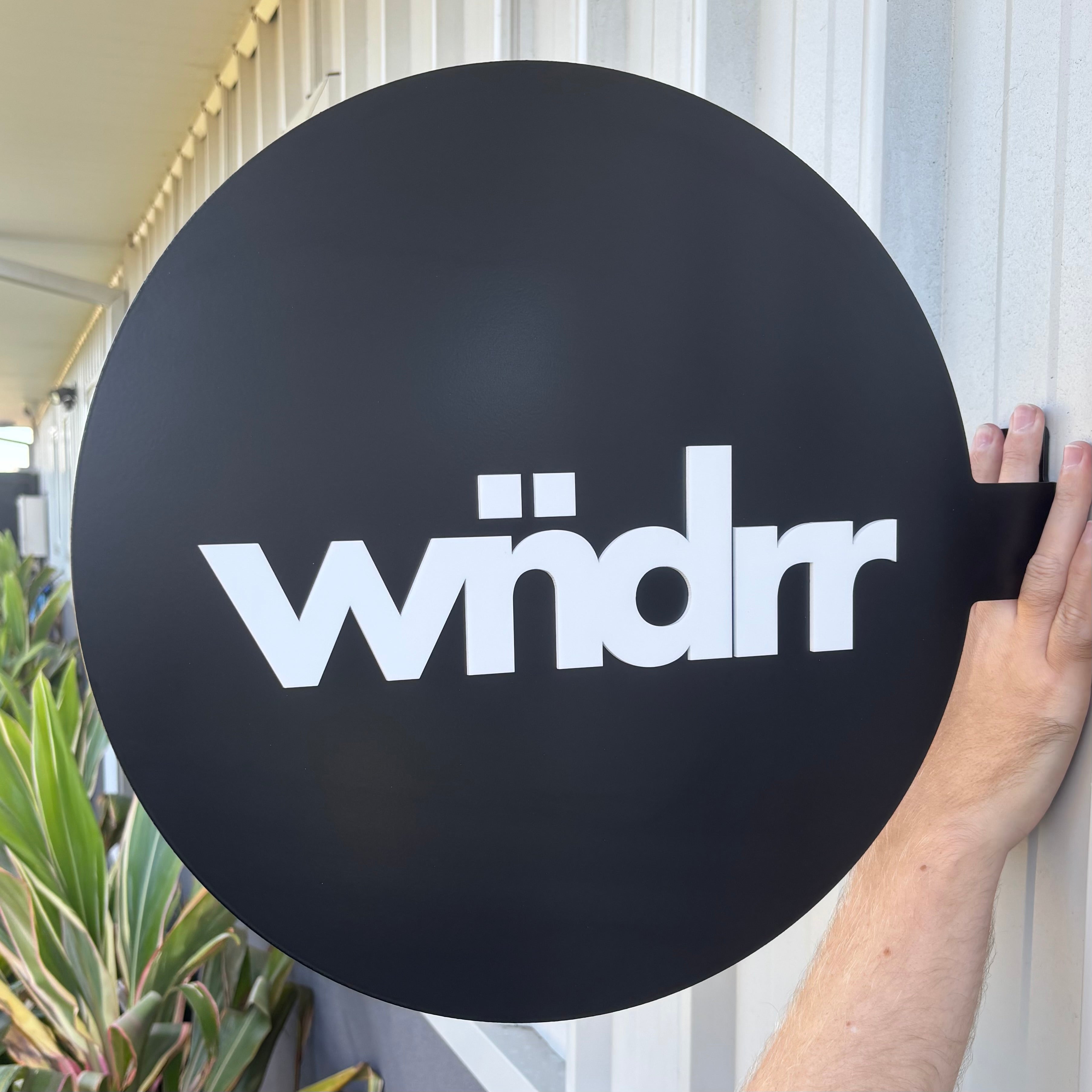 Round blade sign with matte black finish and white logo lettering, custom acrylic business signage for shopfronts, double-sided projecting wall sign for salons, retail and cafés, modern exterior branding sign Australia-made