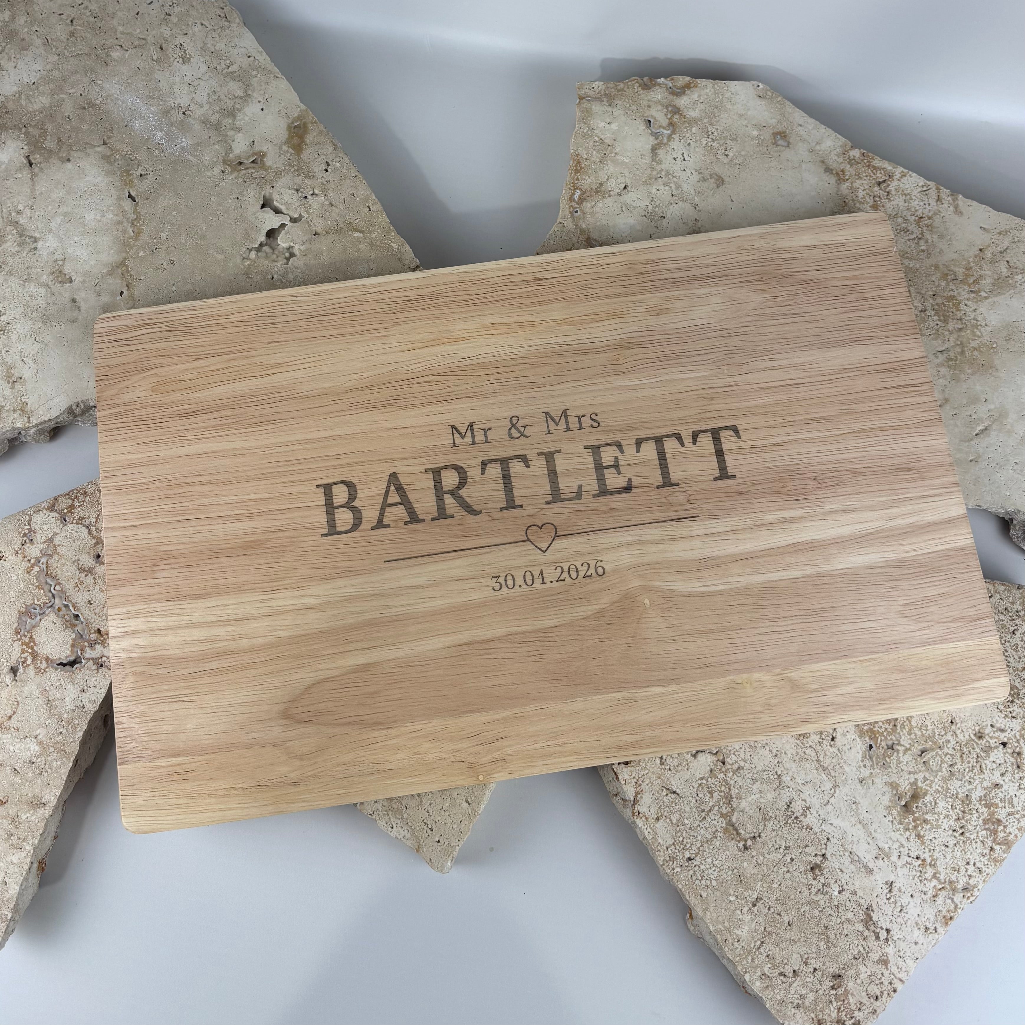 Personalised engraved wooden chopping board reading “Mr & Mrs Bartlett” with wedding date, featuring natural timber grain and styled on a neutral stone background