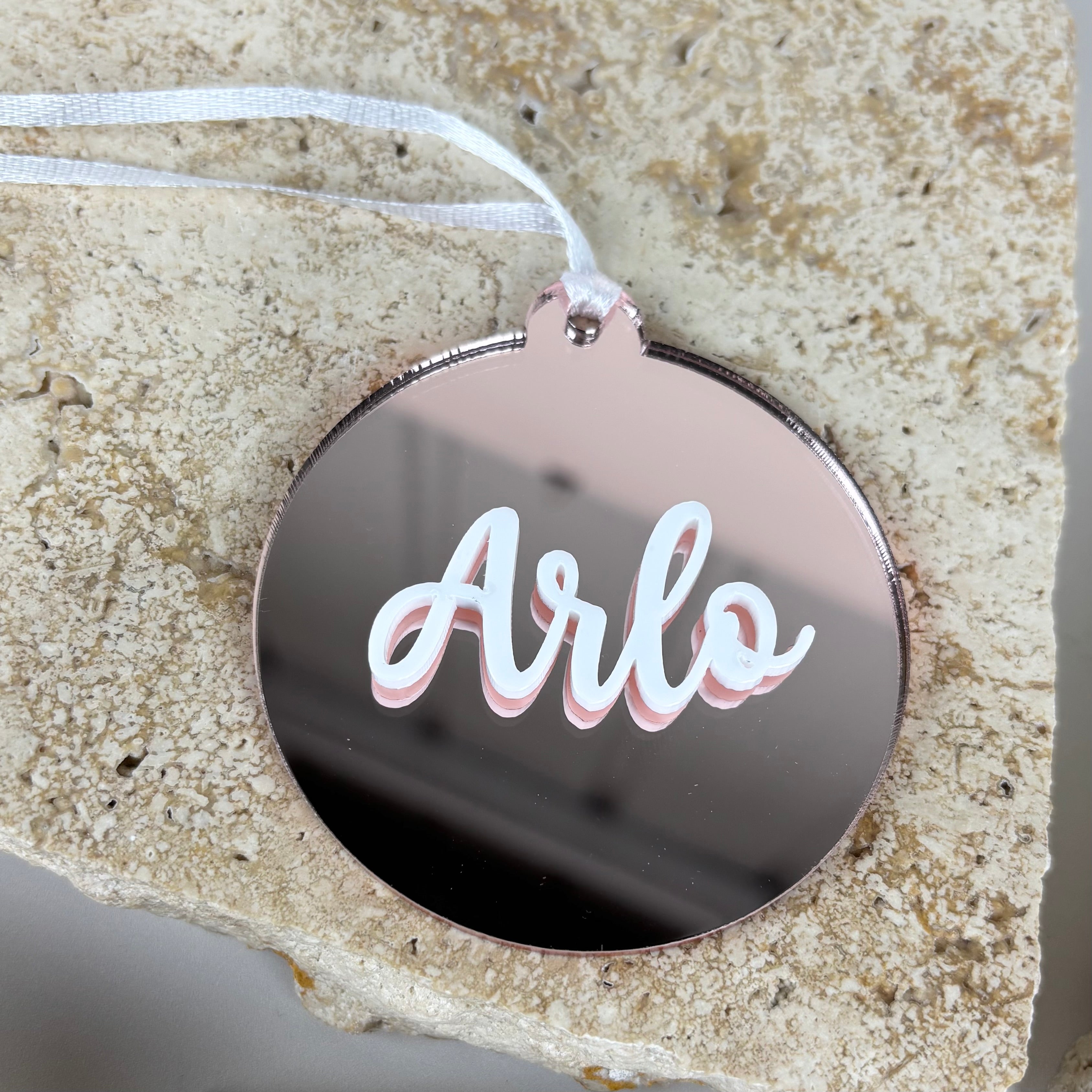 personalised rose gold acrylic christmas bauble with white layered name arlo displayed on stone background, custom mirror ornament holiday decoration australia made gift tag keepsake