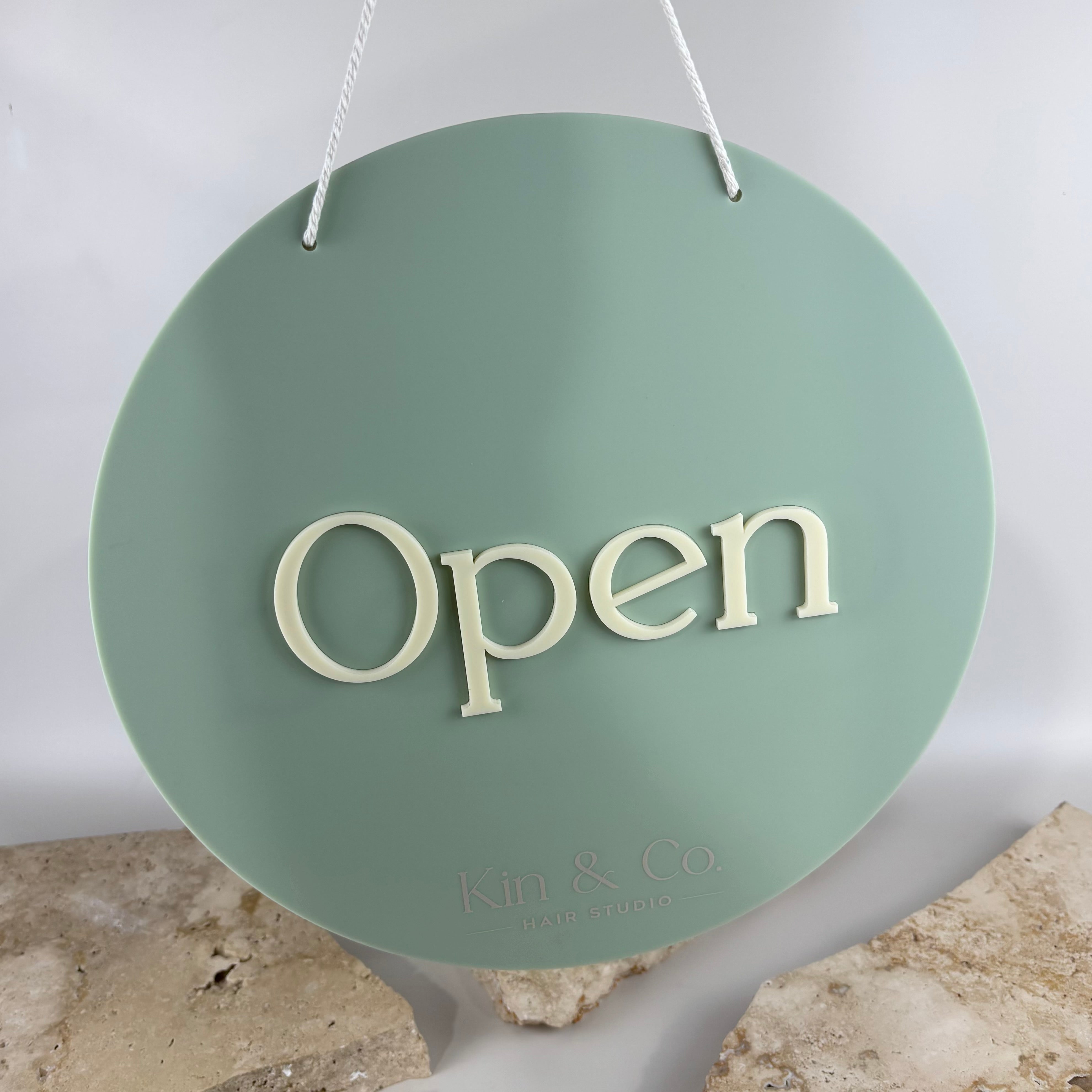 Custom round hanging open sign with raised white 3D acrylic lettering on a sage green acrylic background, personalised business door sign for hair salons, beauty salons, barbers, boutiques and retail shops.
