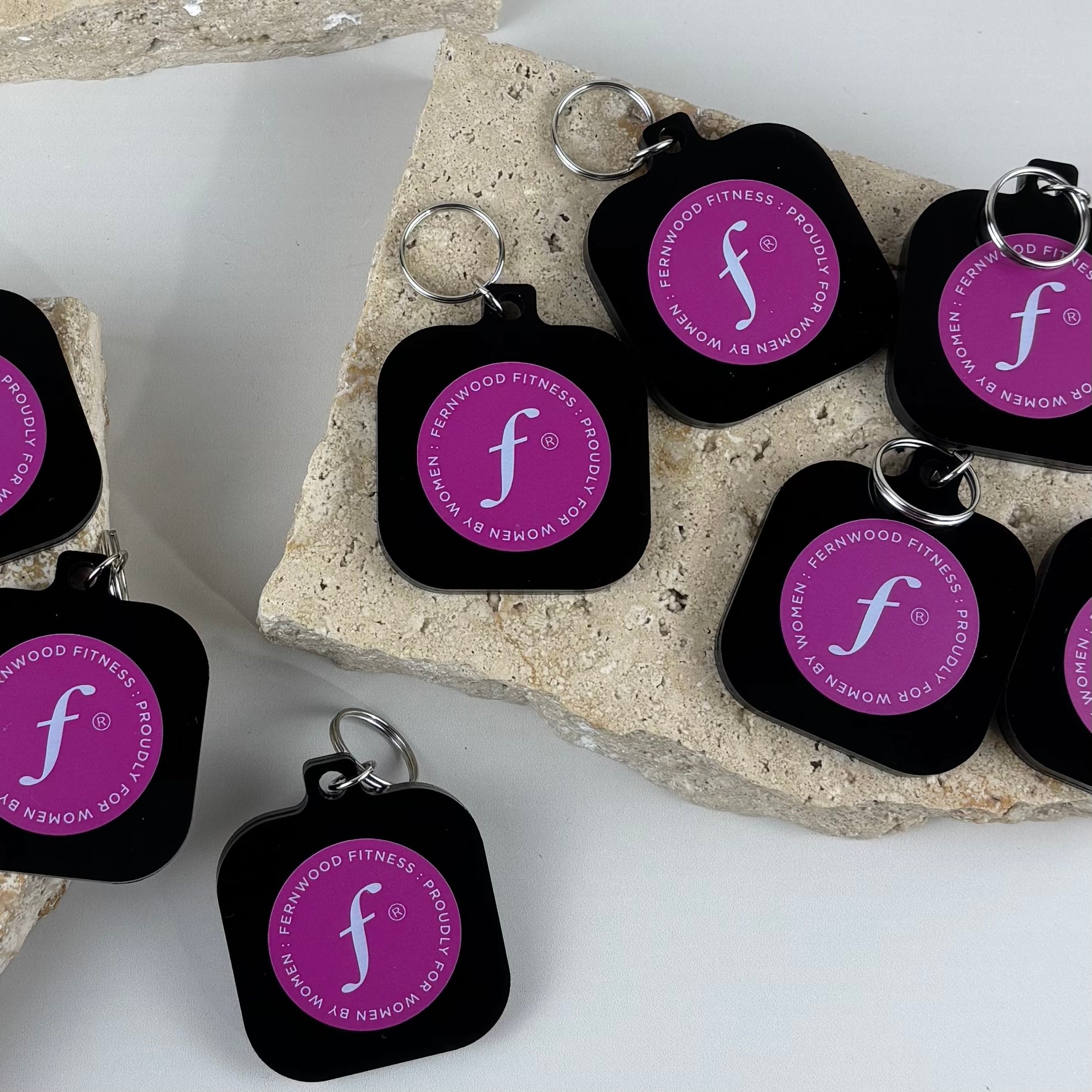 Custom black acrylic NFC keychains with UV printed Fernwood Fitness branding in pink and white for contactless digital access.