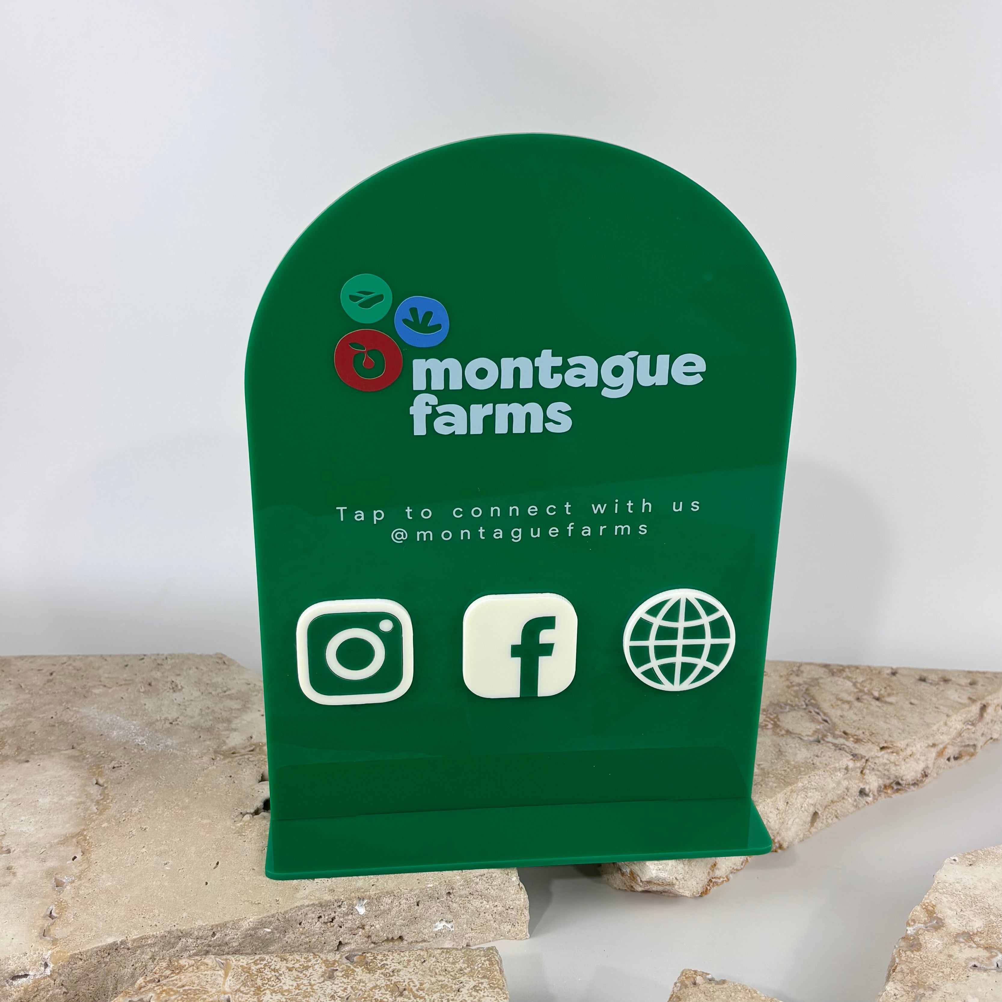 Custom green acrylic NFC business stand featuring the Montague Farms logo with Instagram, Facebook and website icons. UV printed countertop social media sign with embedded NFC technology for instant tap-to-connect, ideal for retail stores, farm shops, markets and business displays