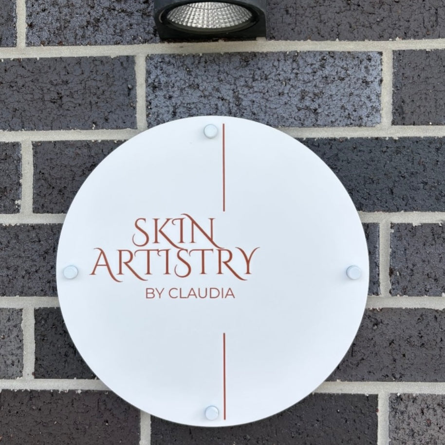 Custom round frosted acrylic business sign mounted on brick wall, Skin Artistry by Claudia logo signage, modern beauty salon exterior sign Australia, UV printed acrylic sign with stand-offs, minimalist clinic branding display
