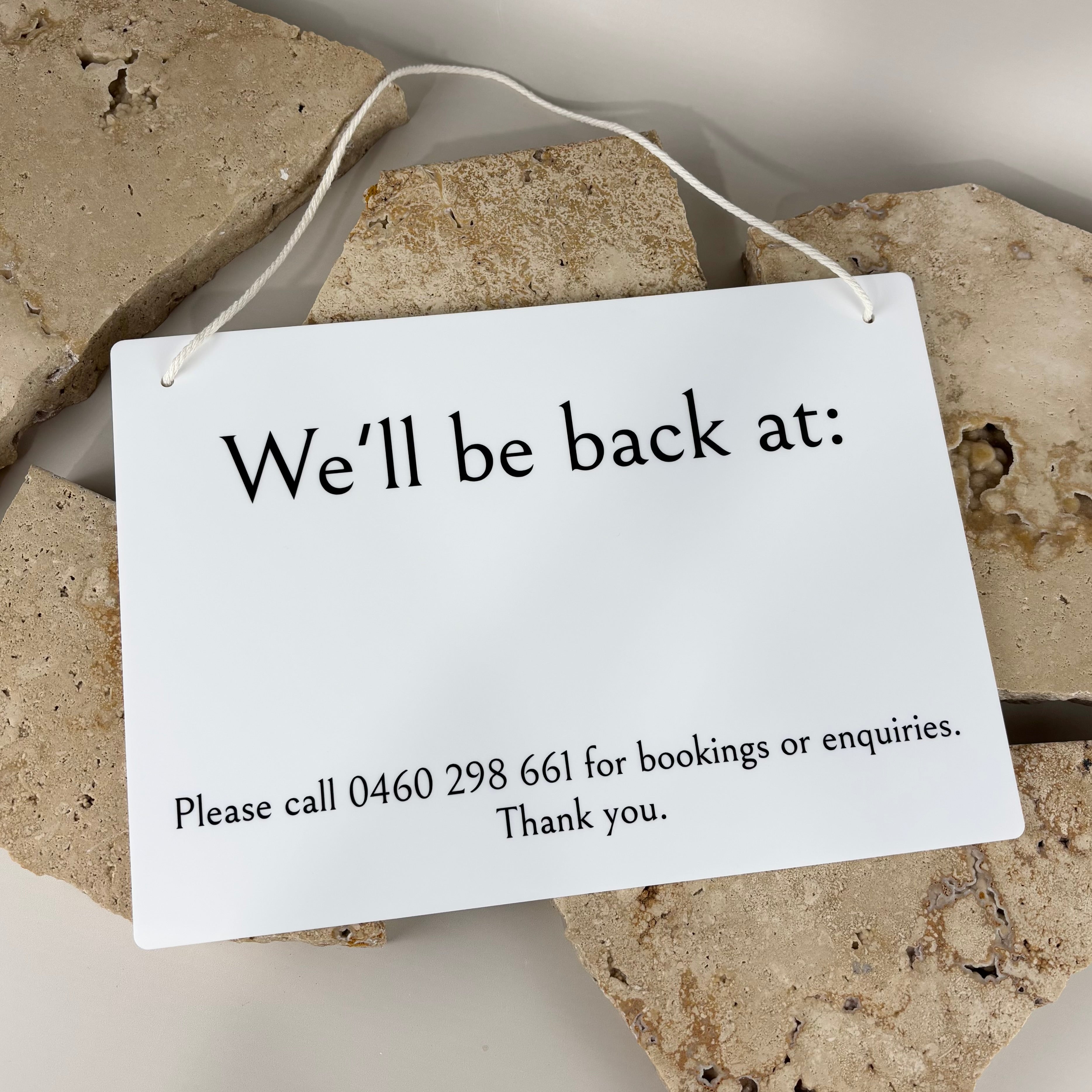 white acrylic business sign with hanging cord displaying “we’ll be back at:” and booking phone number, modern black lettering, salon and beauty clinic closed return time signage for storefront doors australia