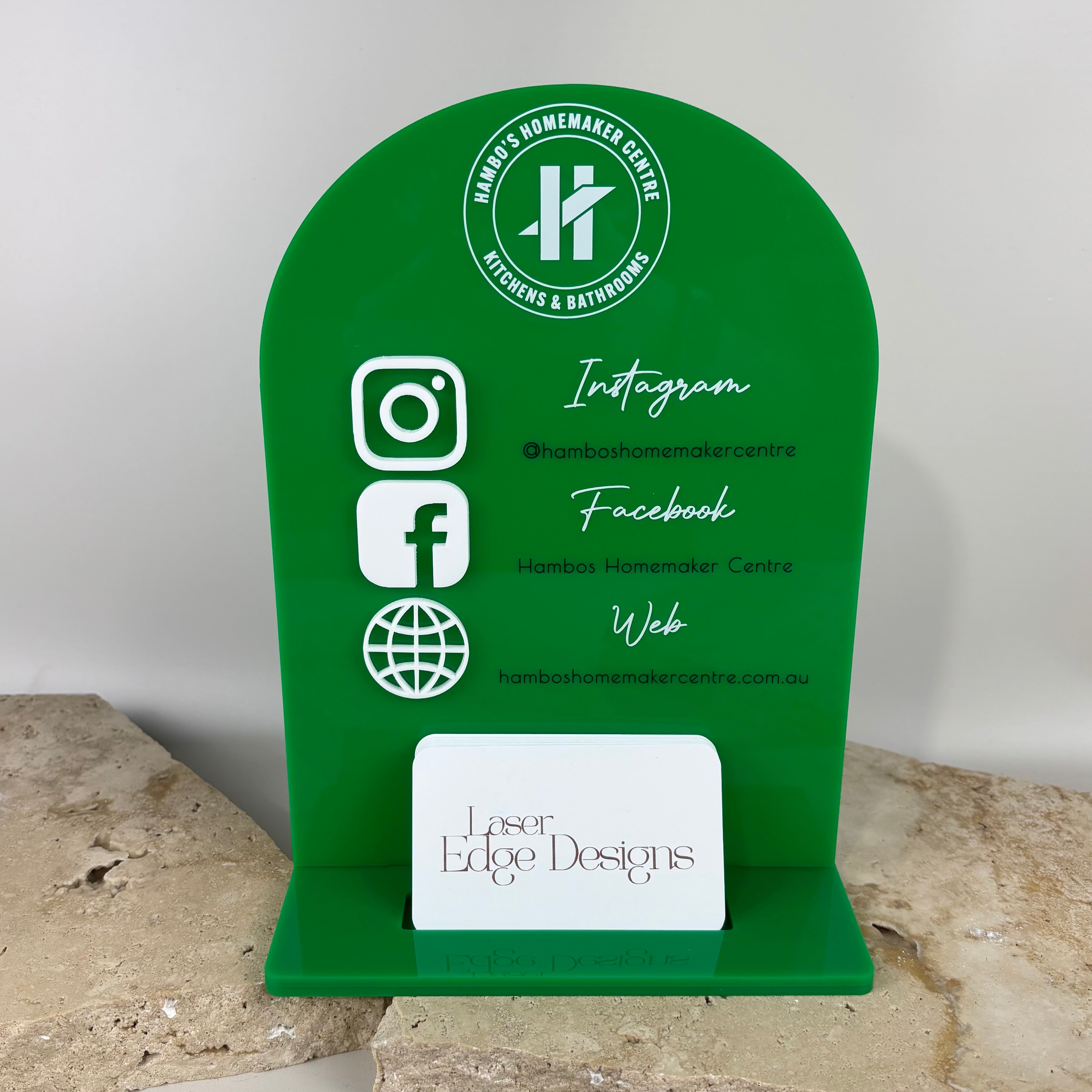 Green acrylic arch business stand with social media icons and website details, including business card holder, branded for Hambos Homemaker Centre kitchens and bathrooms, styled on stone tiles