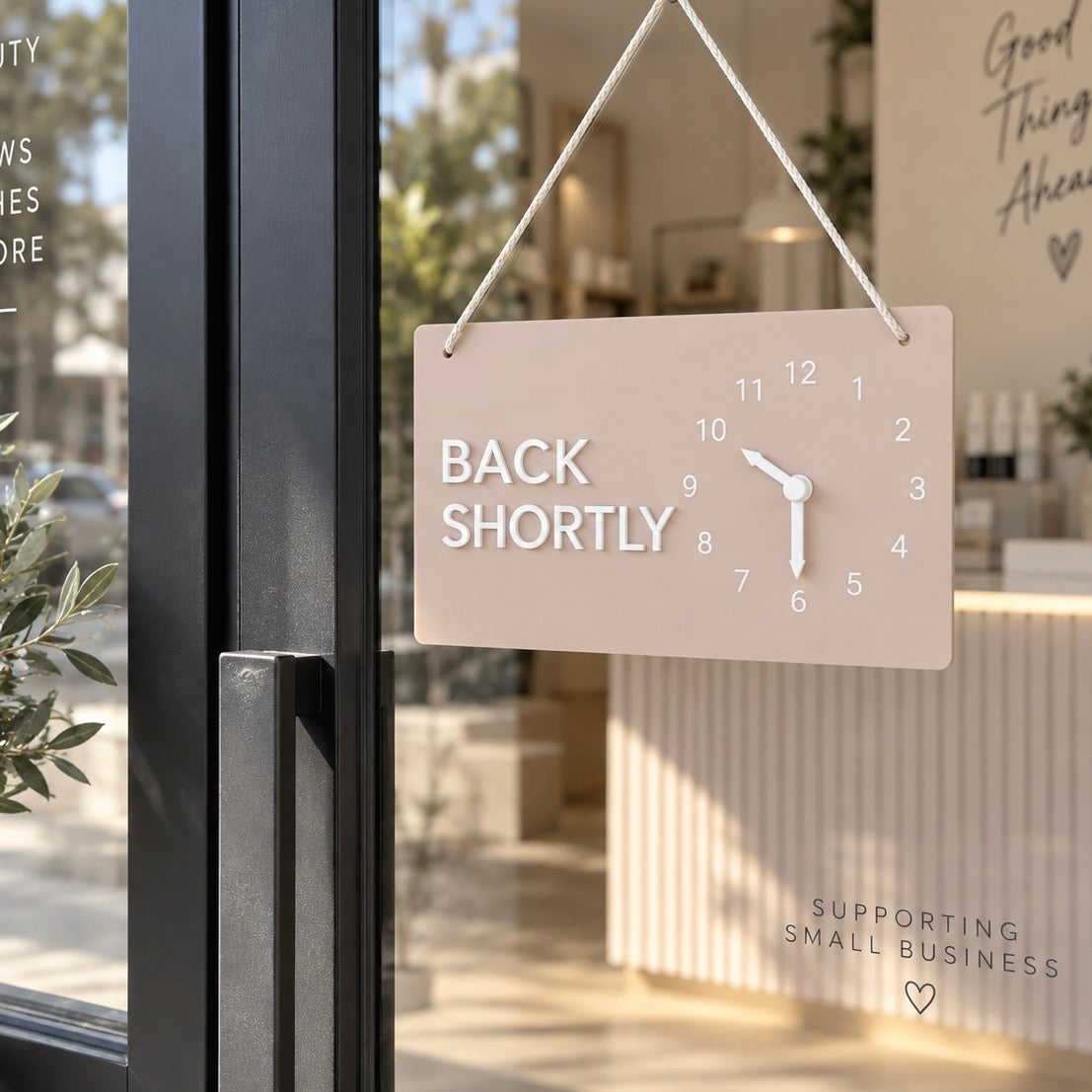 Back Shortly acrylic business door sign with movable clock hands displayed on a modern salon shopfront.