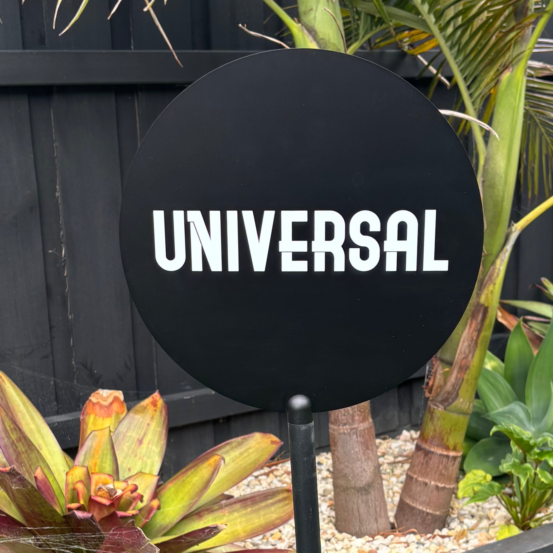 Black powder coated metal floor stand with round business logo sign, bold white lettering on circular panel, professional freestanding branding signage for shopfronts and events