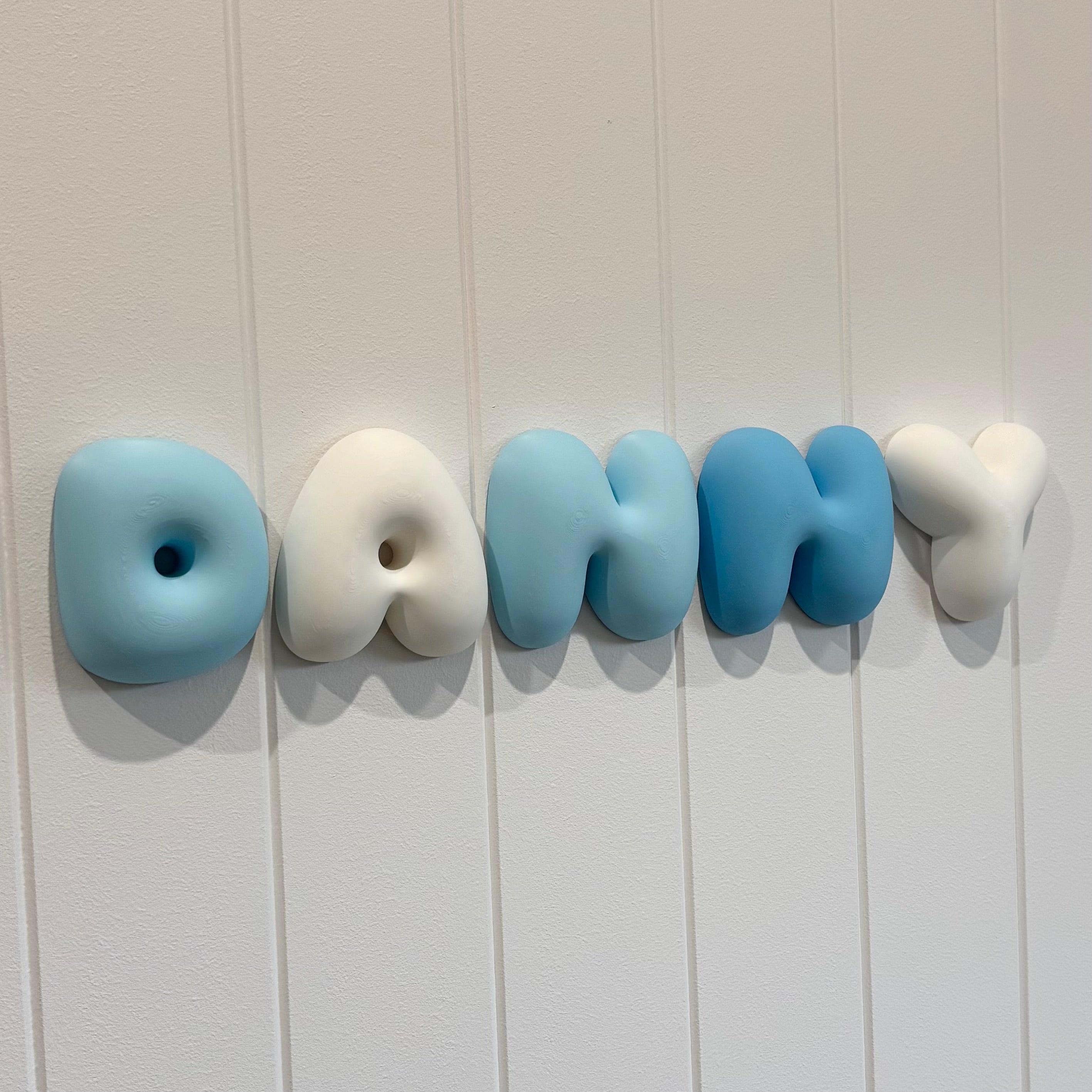 Custom 3D bubble name wall sign spelling “Danny” in alternating blue and white PLA letters, creating a playful, modern personalised bedroom or nursery wall decoration with a soft sculptural finish.