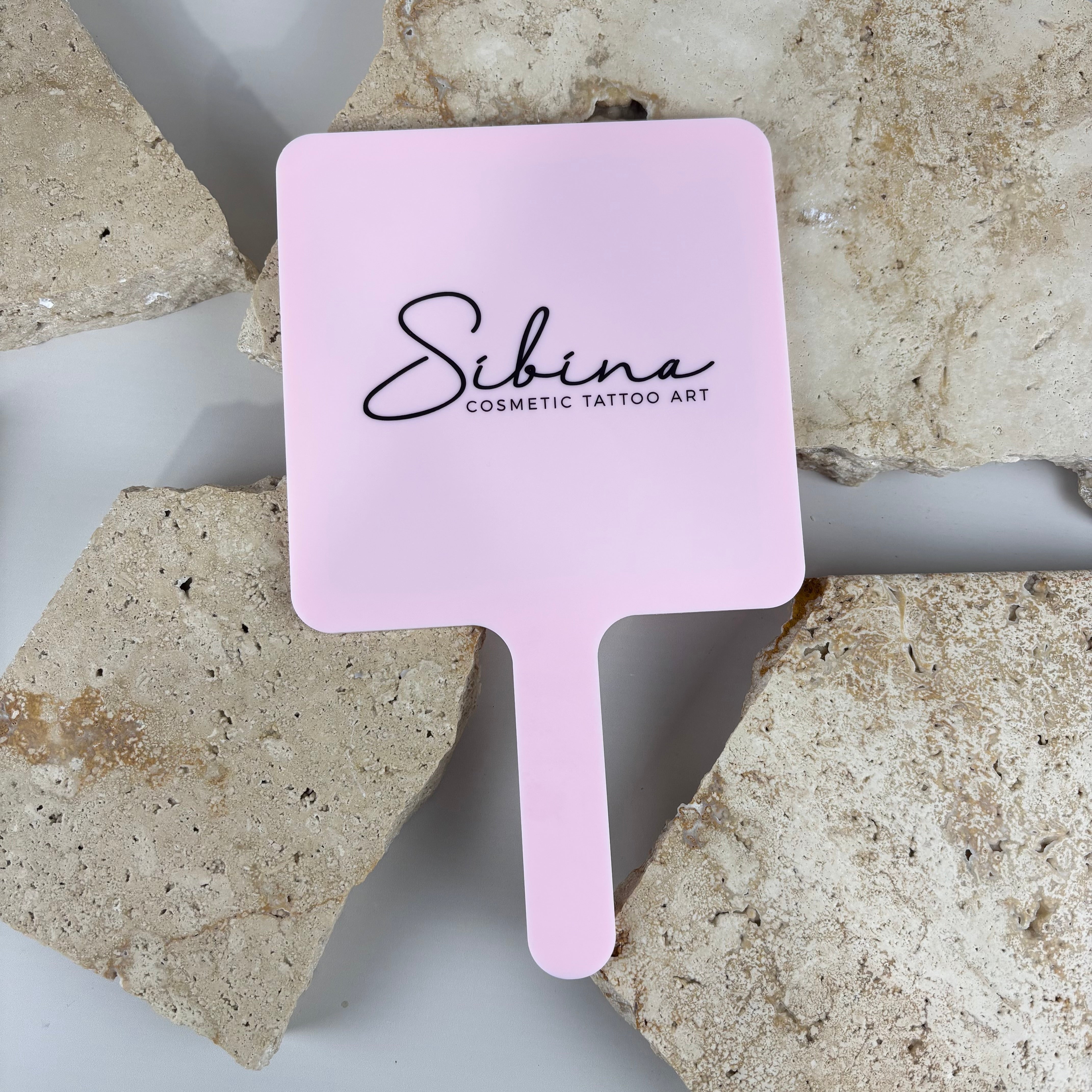 Pink acrylic handheld salon mirror with black logo branding, custom hairdressing mirror designed for beauty salons, cosmetic tattoo artists and aesthetic clinics to show clients finished results.