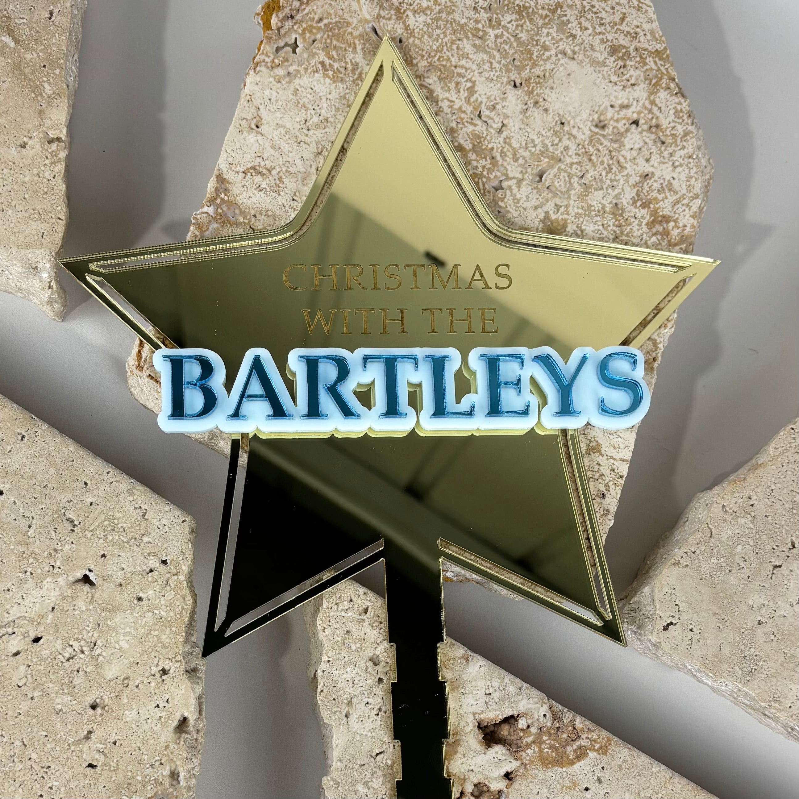 Gold mirrored acrylic star Christmas tree topper personalised with raised blue family name “Bartleys” and engraved text “Christmas with the Bartleys”, layered custom acrylic star topper for Christmas trees.