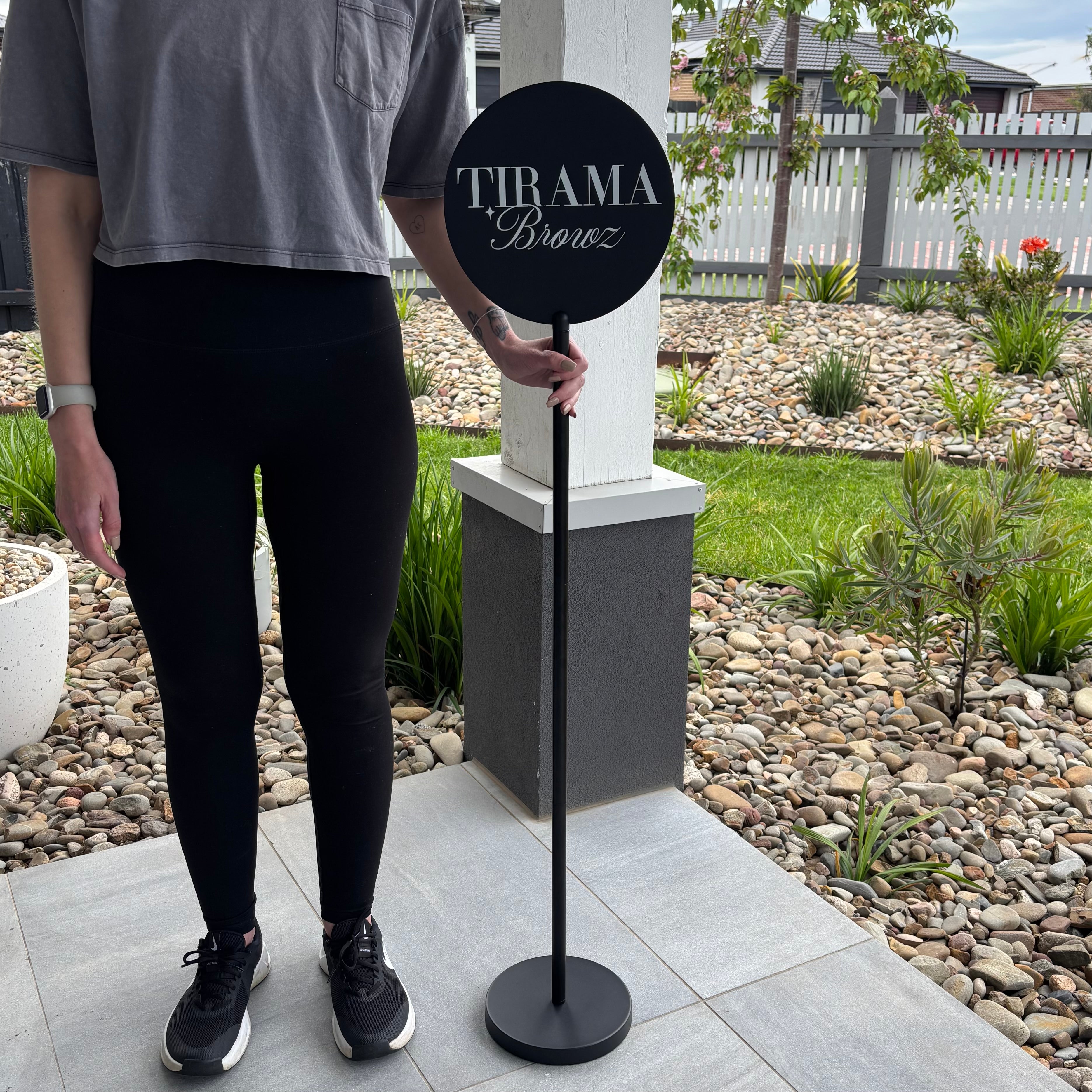 Custom round acrylic business sign on a freestanding floor stand for beauty salons and brow studios.