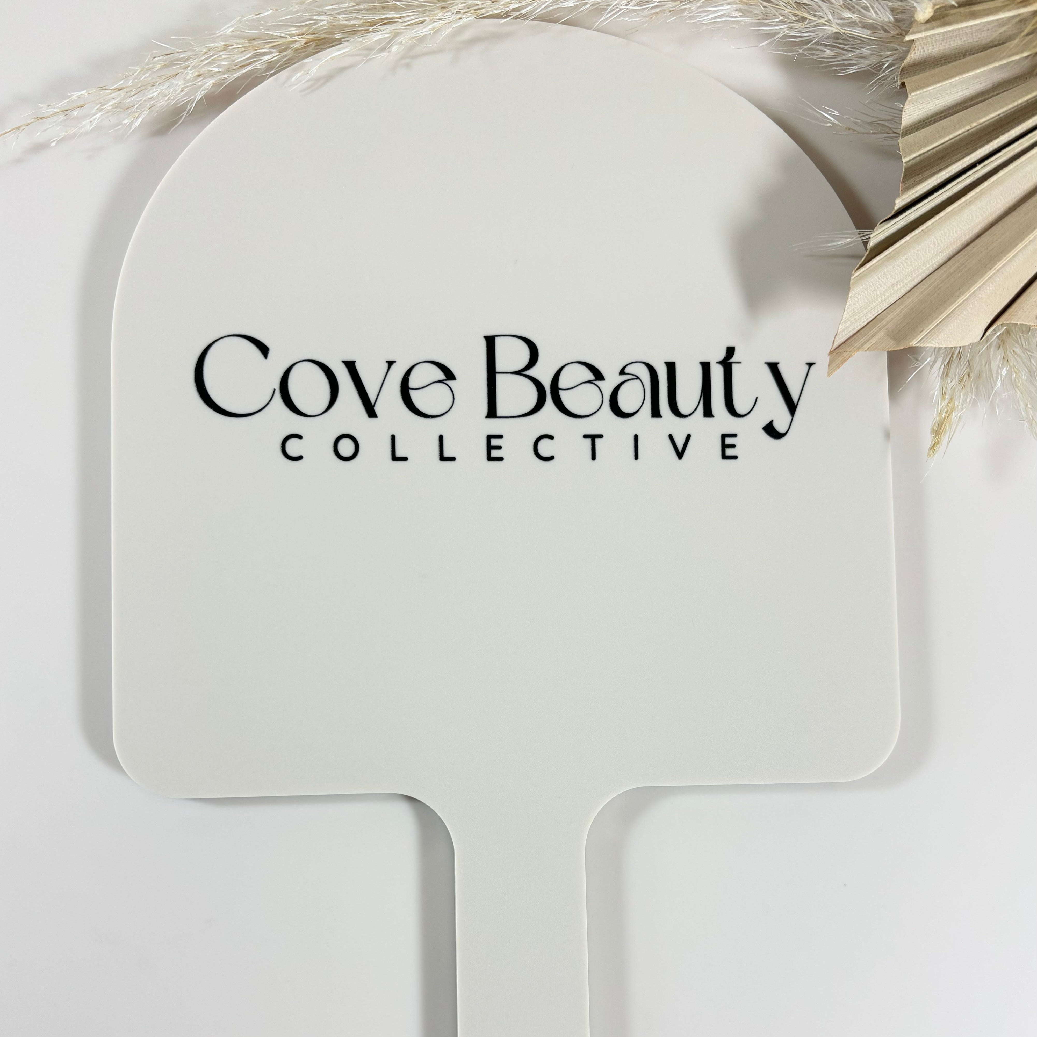 Cove Beauty Collective logo on white arched handheld mirror