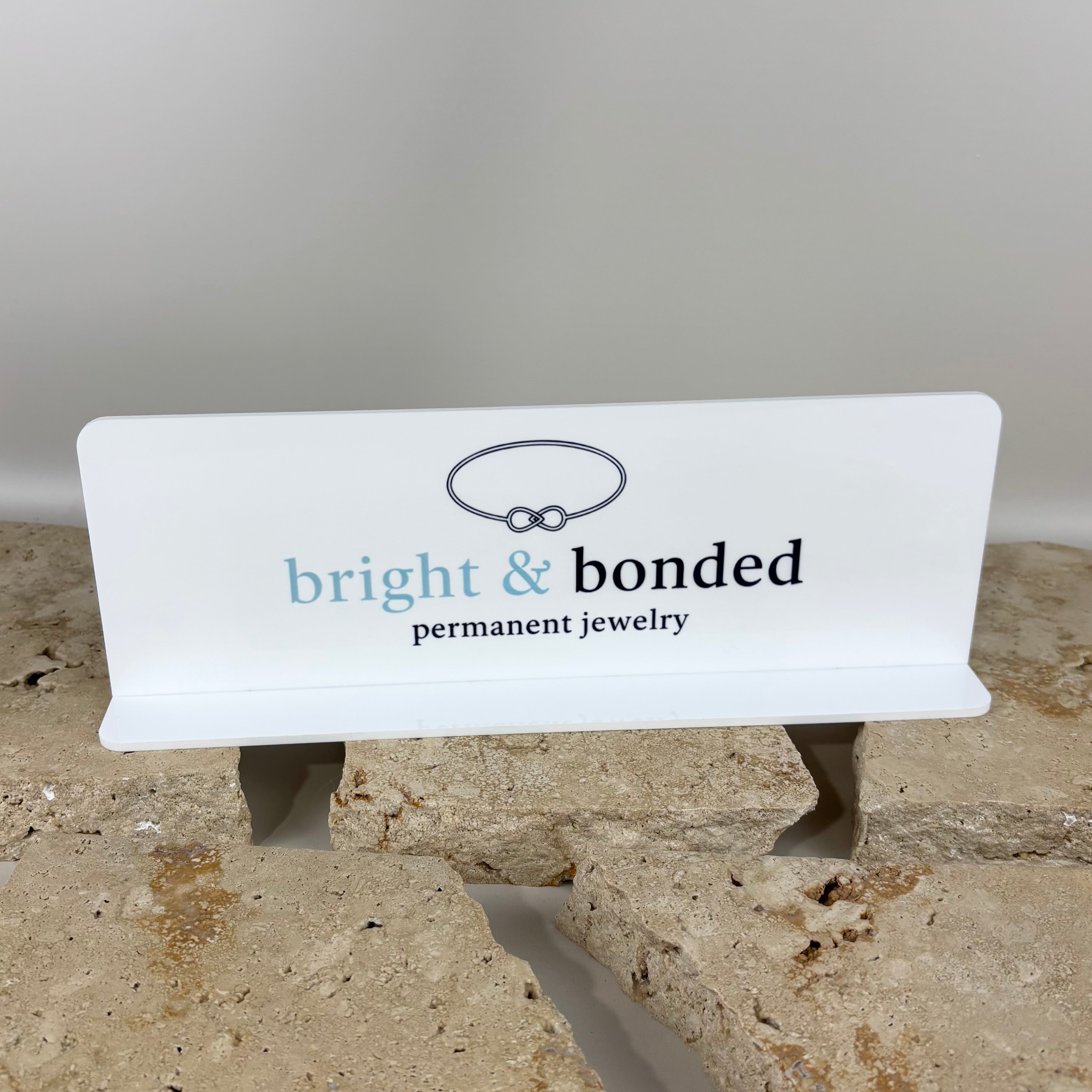 White acrylic permanent jewelry display stand with custom logo, countertop business signage for permanent jewelry artists, salons, markets and pop-up stores.