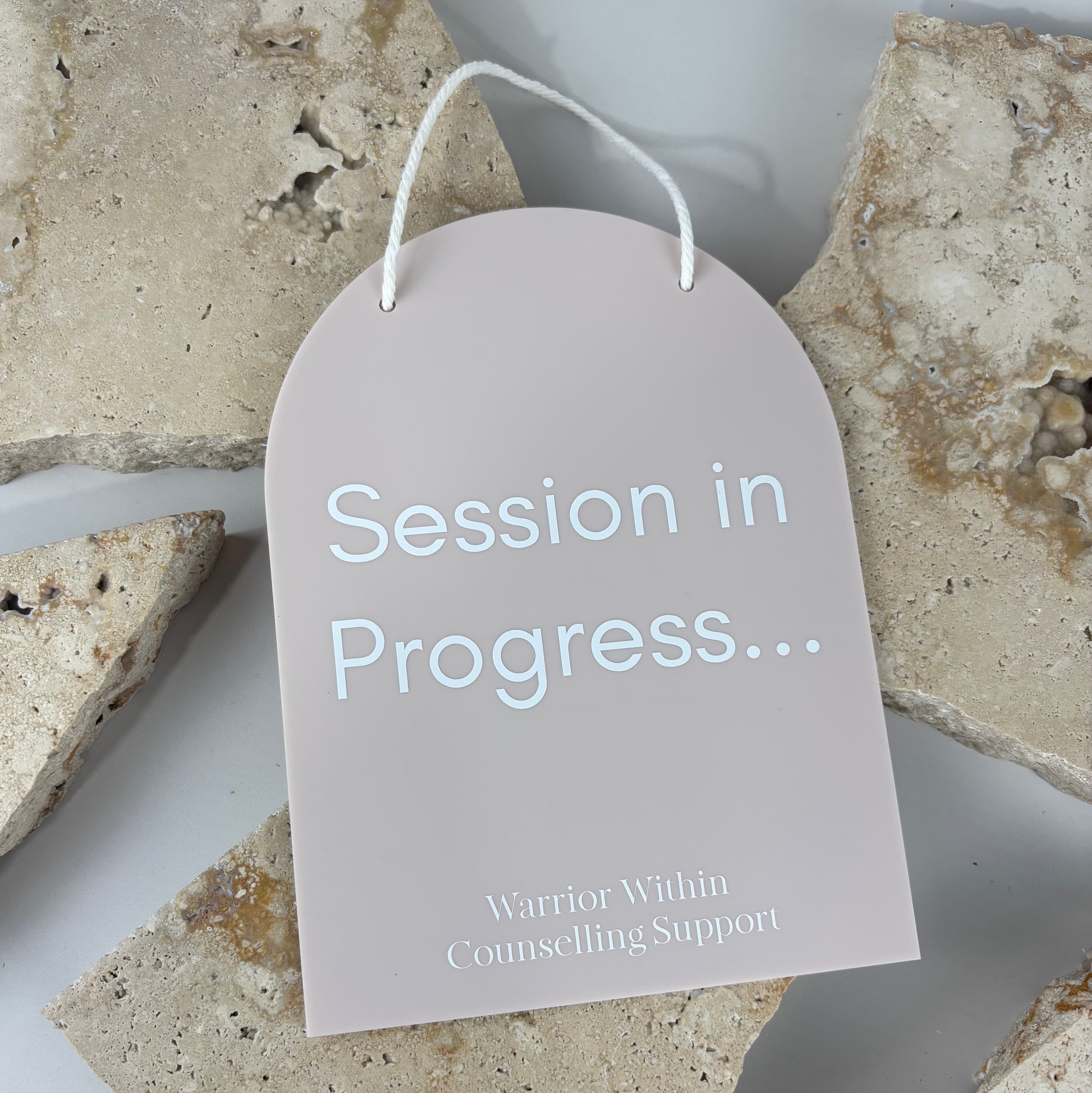 Custom acrylic door sign reading “Session in Progress” for counselling and therapy rooms, featuring a soft blush arch design with white raised lettering and rope hanger.