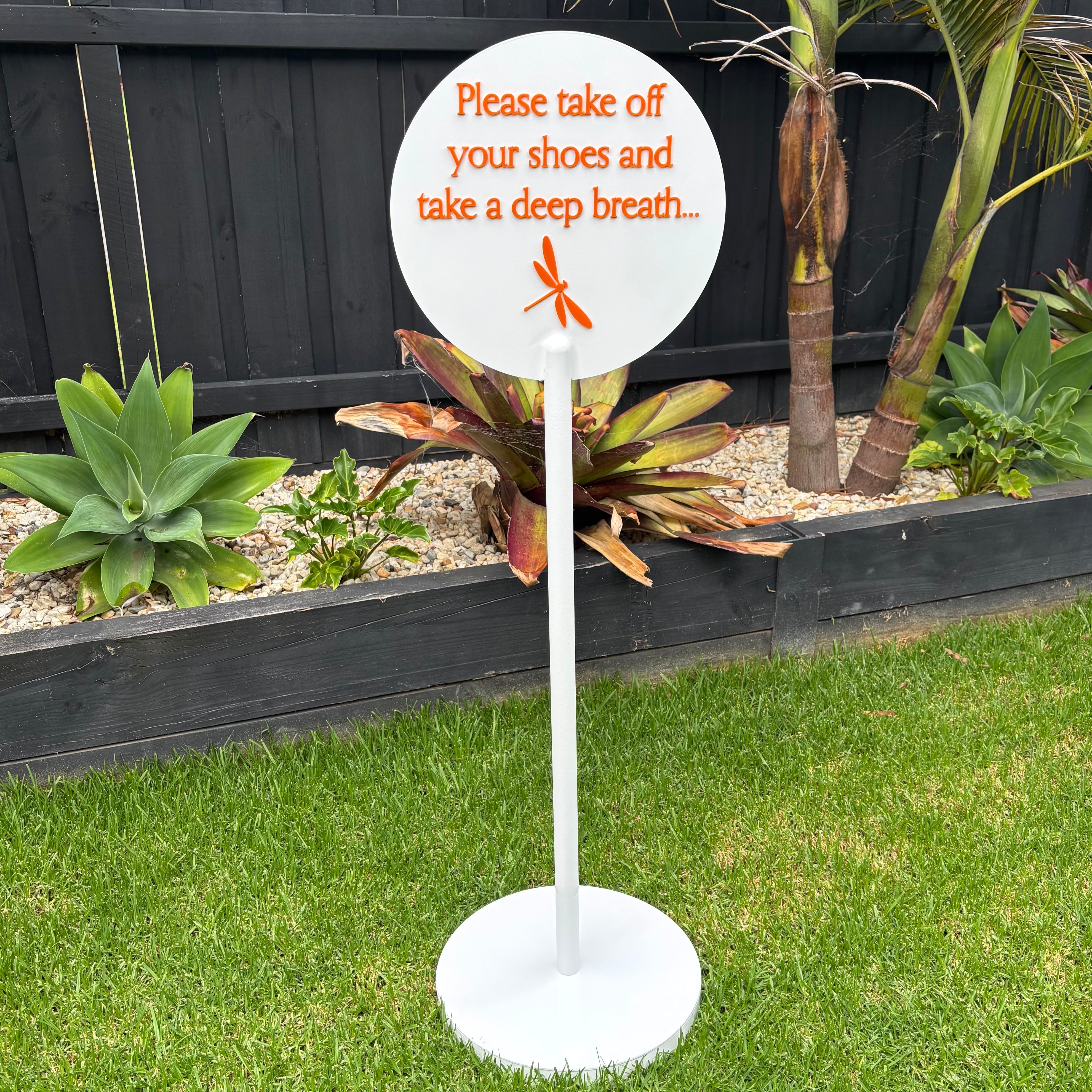 Custom round acrylic outdoor sign on stand with raised 3D lettering “Please take off your shoes and take a deep breath”, white matte finish with orange acrylic text, modern garden signage, freestanding business or home entry sign