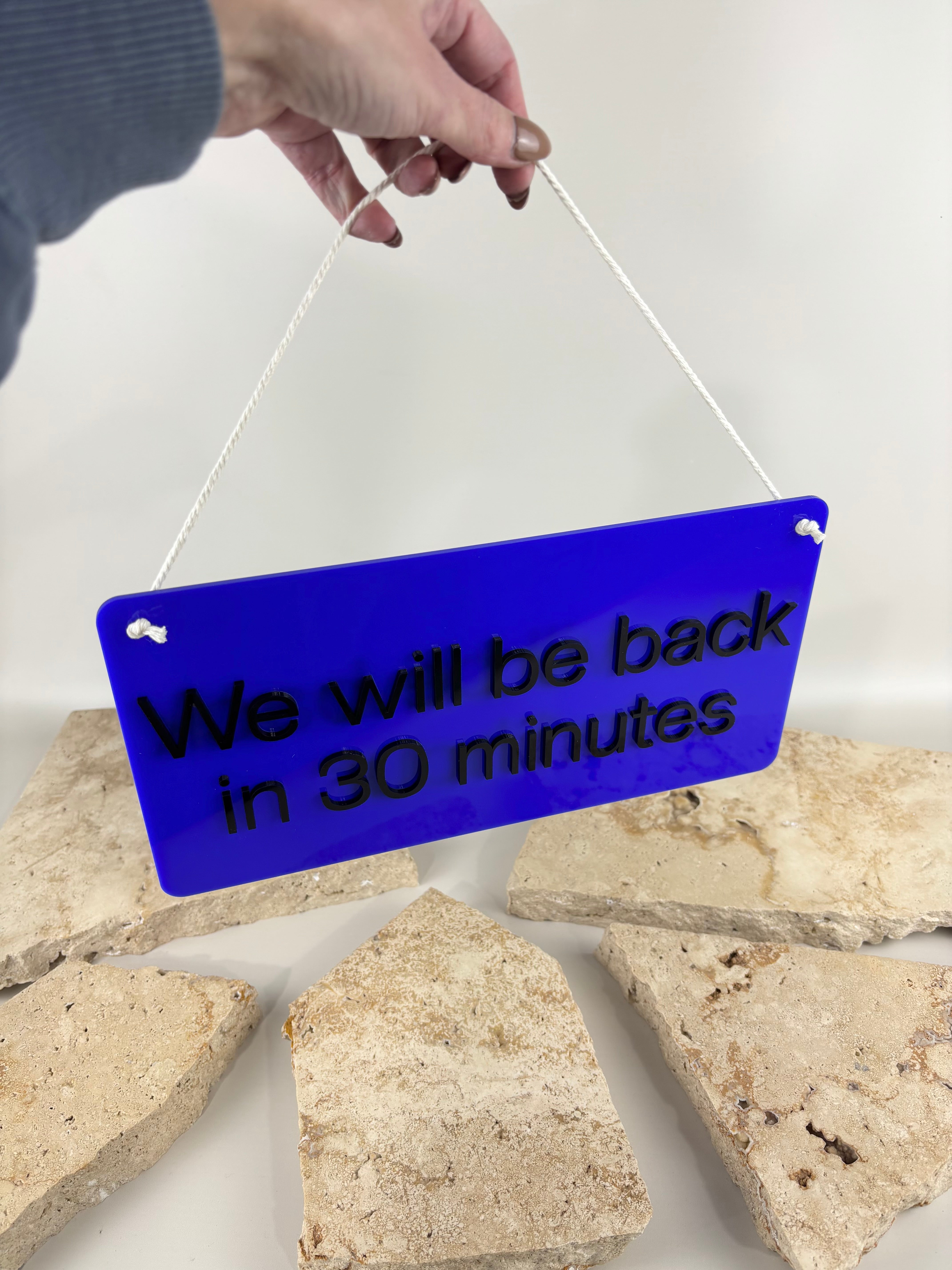 Bright blue acrylic business hanging sign with custom return time message, personalised shop door sign with rope hanger for small businesses, salons, clinics and retail storefront branding.