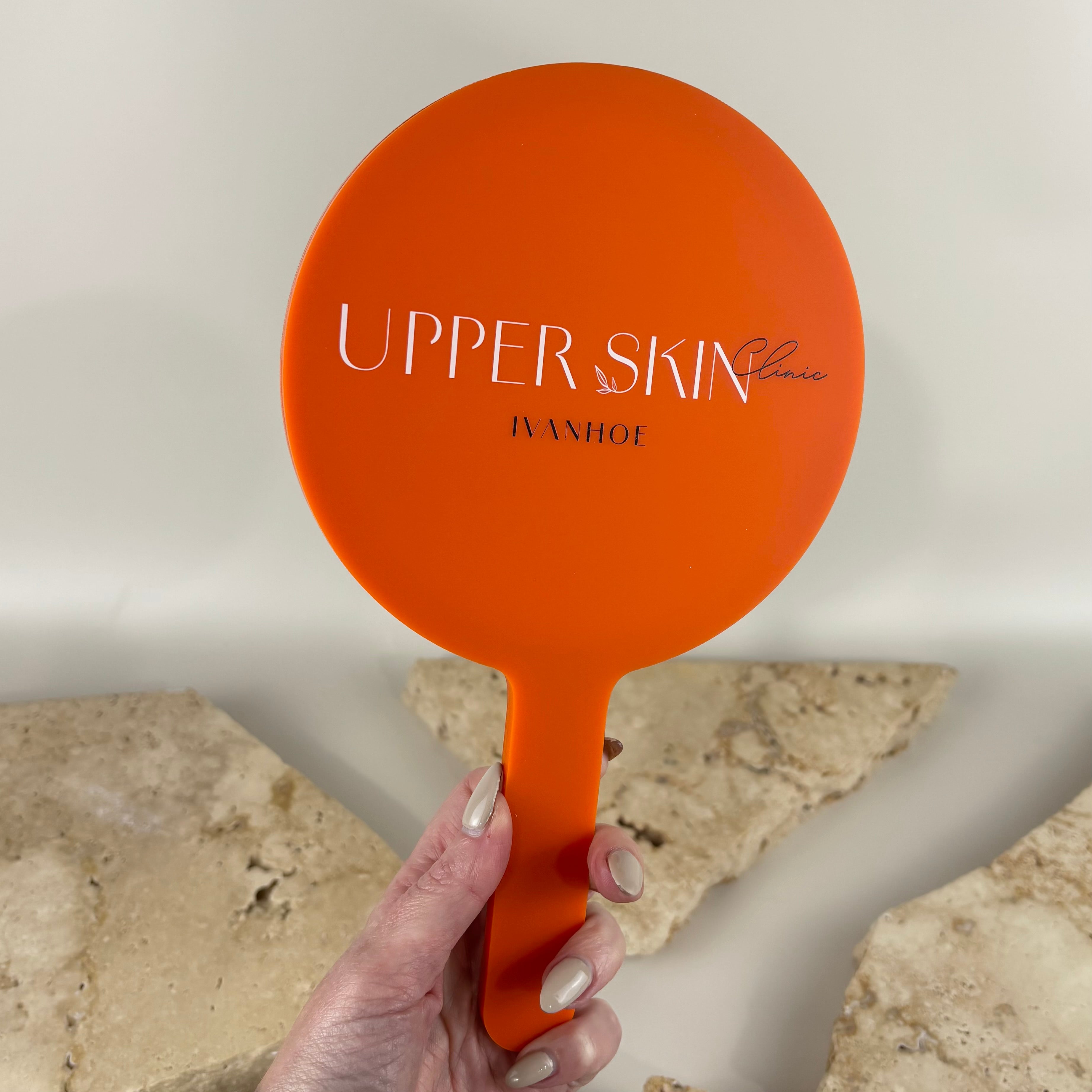Custom bright orange handheld salon mirror with UV printed Upper Skin Clinic Ivanhoe branding. Premium acrylic hand mirror for skin clinics, beauty salons, cosmetic clinics and aesthetic businesses, perfect for client treatments, consultations and branded salon displays.