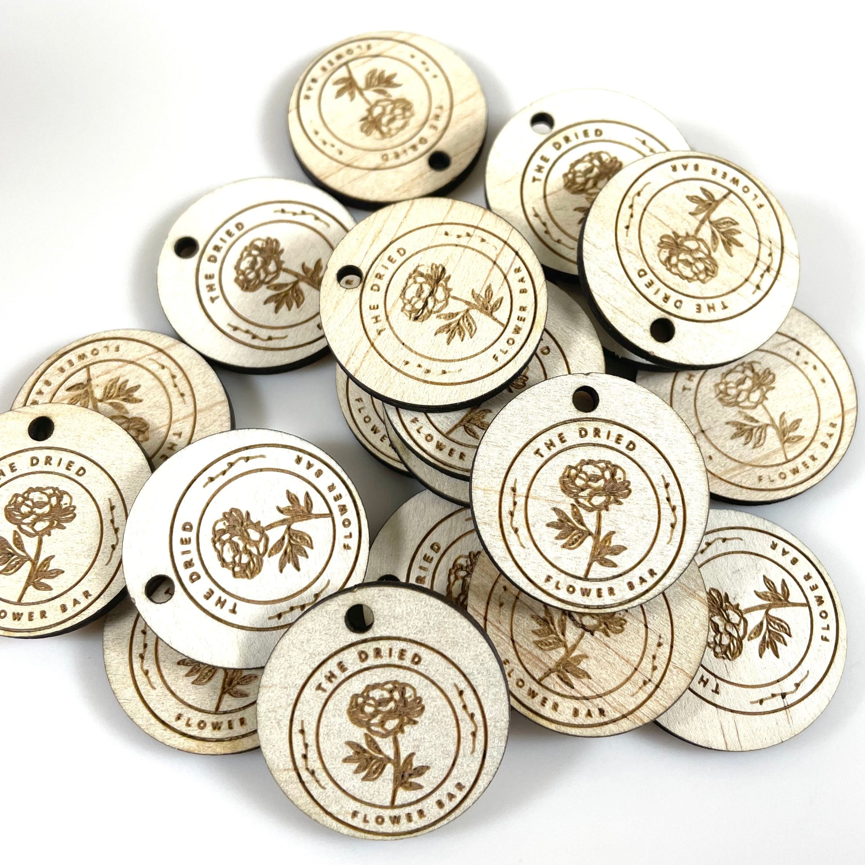 Stack of round timber product tags with floral logo engraving
