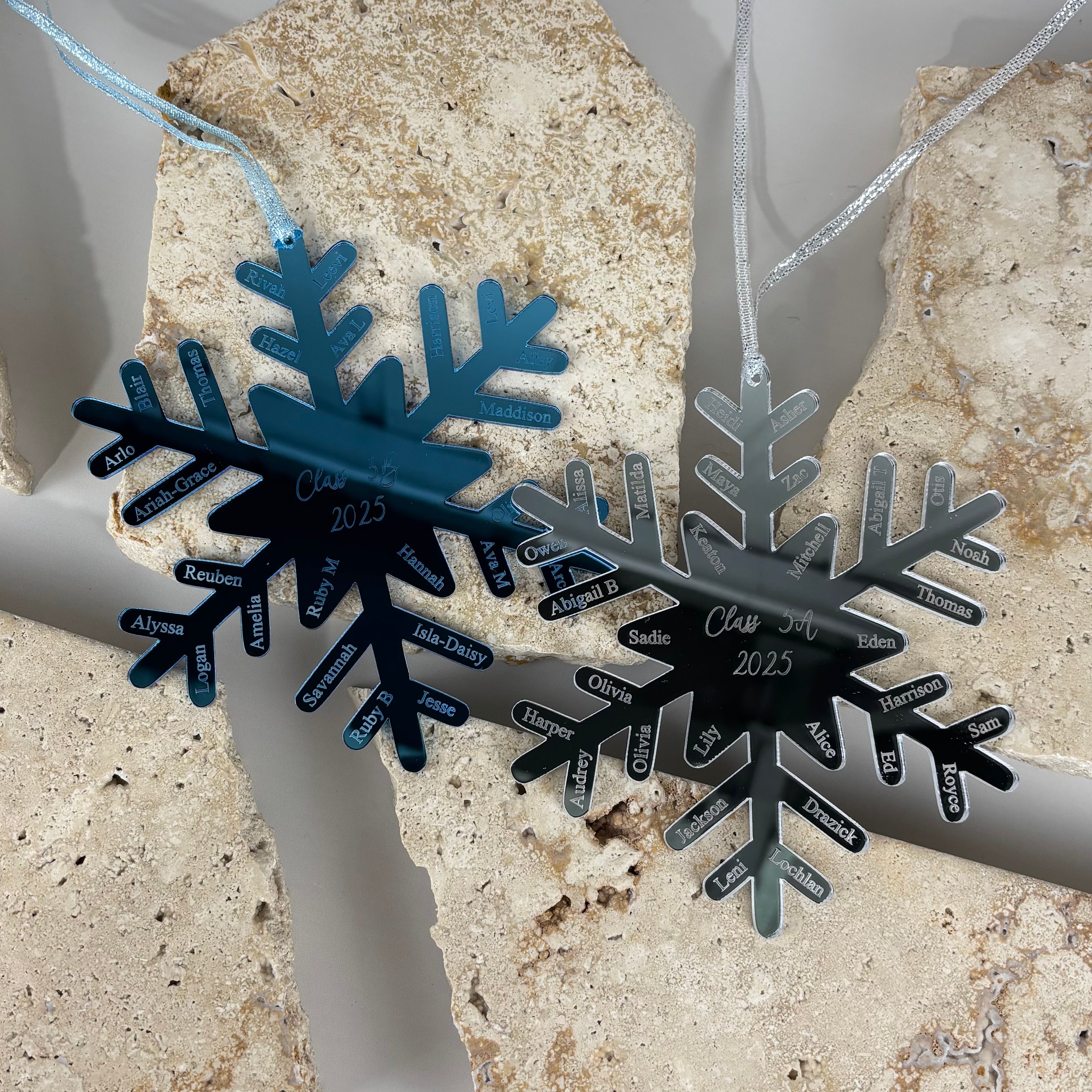 personalised acrylic snowflake christmas ornaments in blue and silver displayed on textured stone background, engraved with class list student names and class of 2025 text, teacher gift school graduation keepsake australia made
