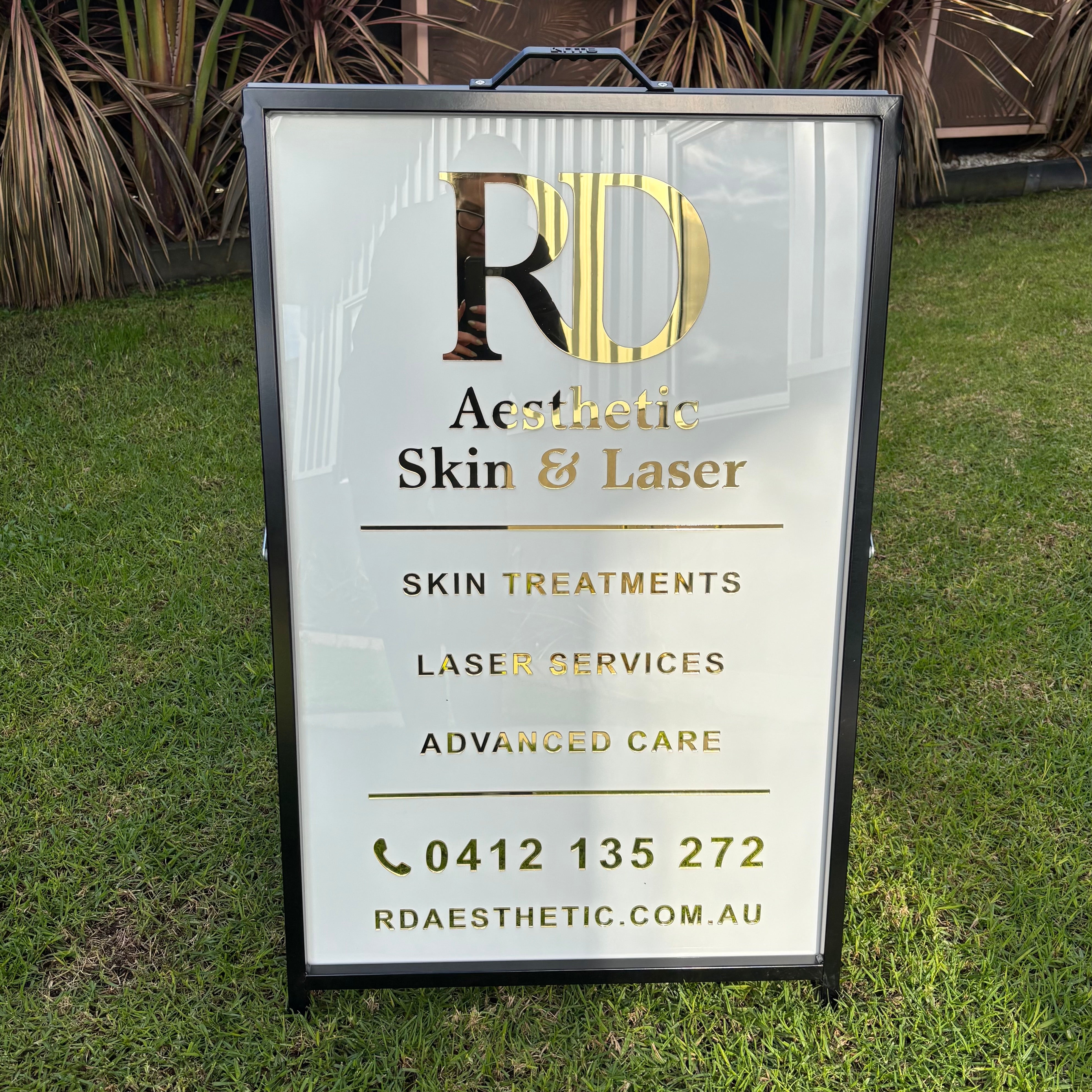 Custom black metal A-frame pavement sign with white acrylic panel and gold mirror 3D lettering for RD Aesthetic Skin & Laser clinic.
