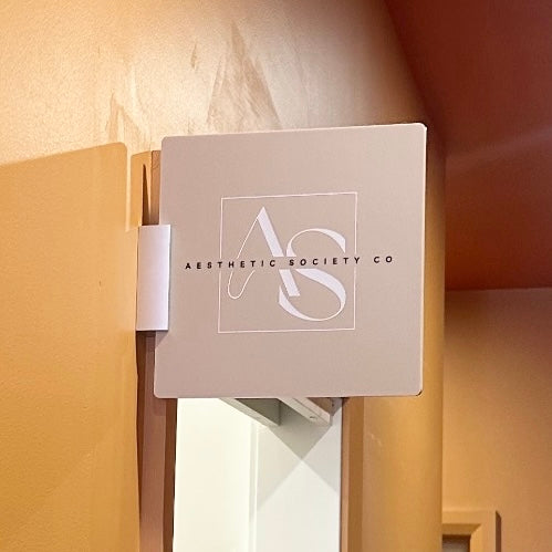 Custom acrylic corridor sign for Aesthetic Society Co in beige with white and black logo, wall-mounted directional signage for salons, clinics, and business branding.