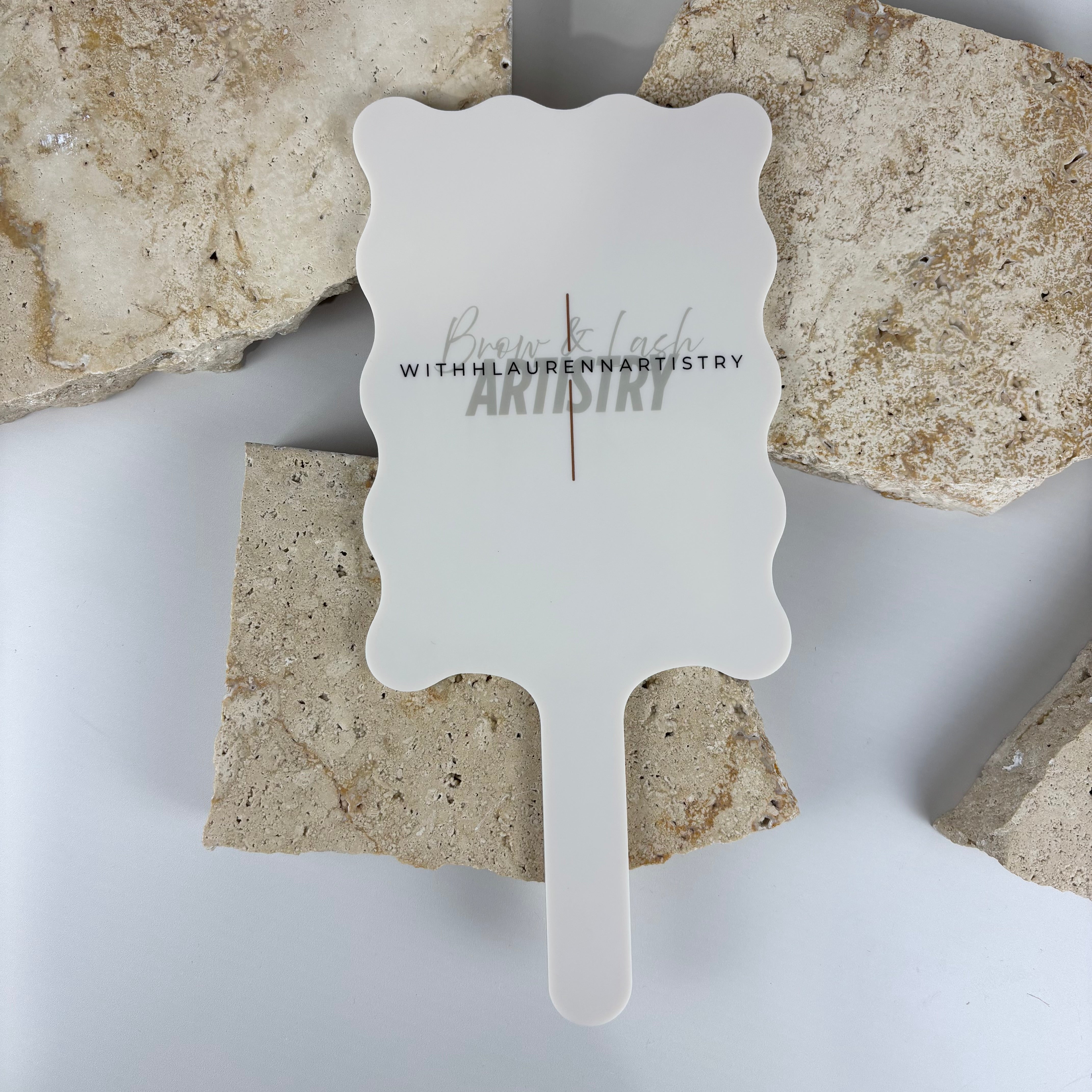 Custom scalloped handheld mirror with engraved logo “Brow & Lash Artistry with Lauren Artistry,” featuring a soft matte white acrylic finish. Perfect for beauty salons, lash and brow artists, or makeup studios wanting branded salon mirrors for client photos and displays.